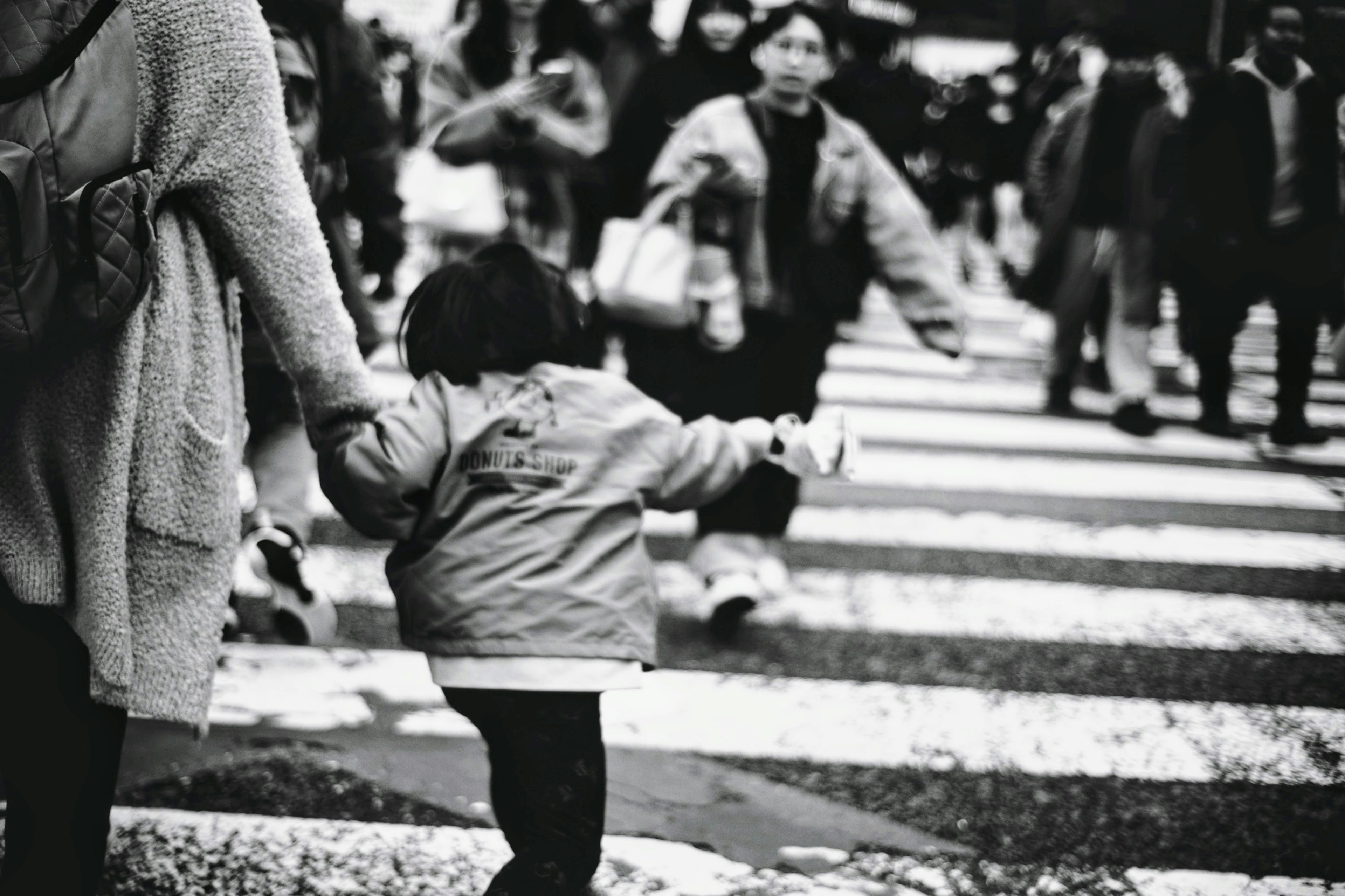 Photo en noir et blanc d'un enfant tenant la main d'un adulte dans un passage piéton animé