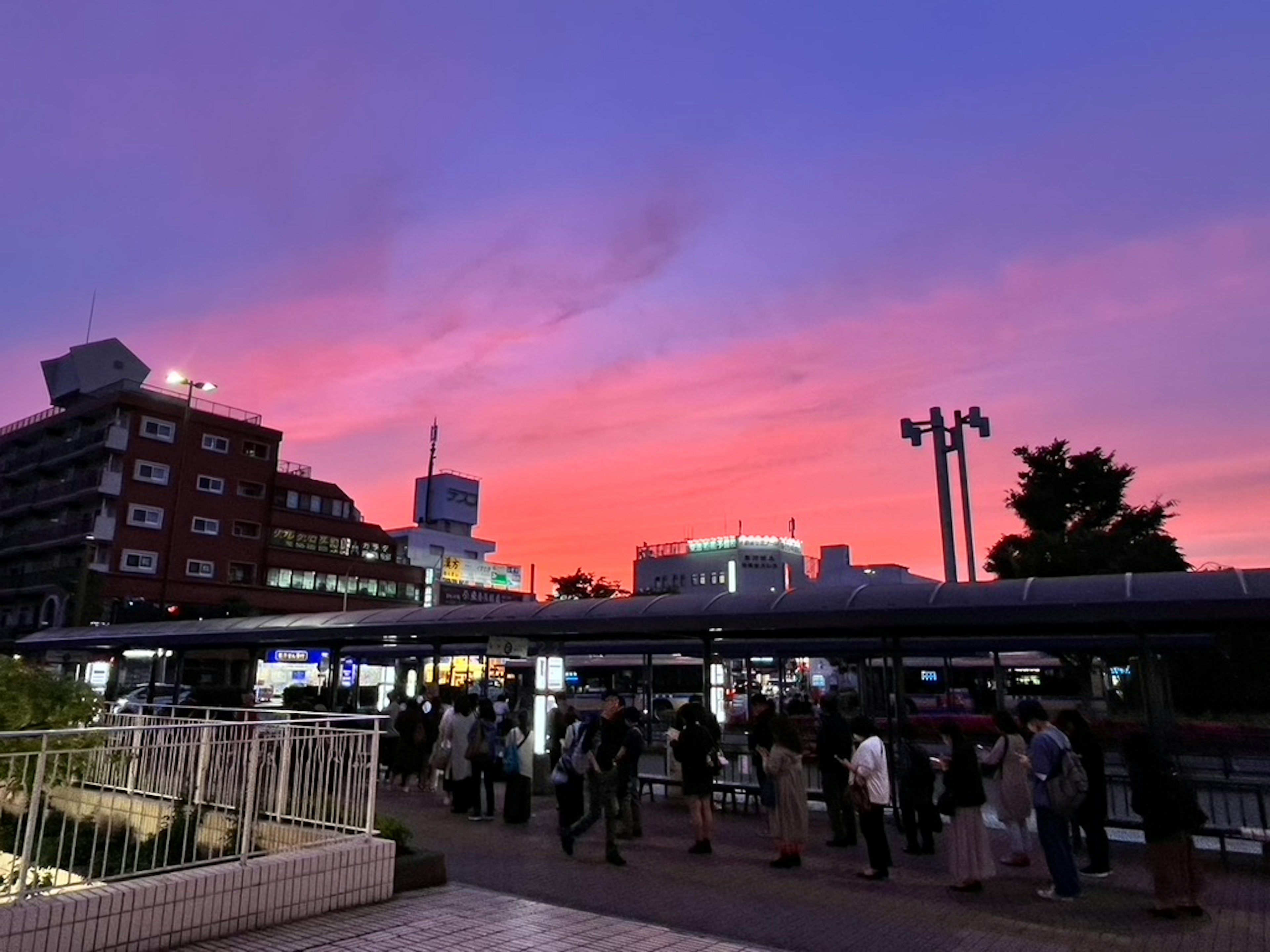 夕焼けの空と人々が集まる駅の風景