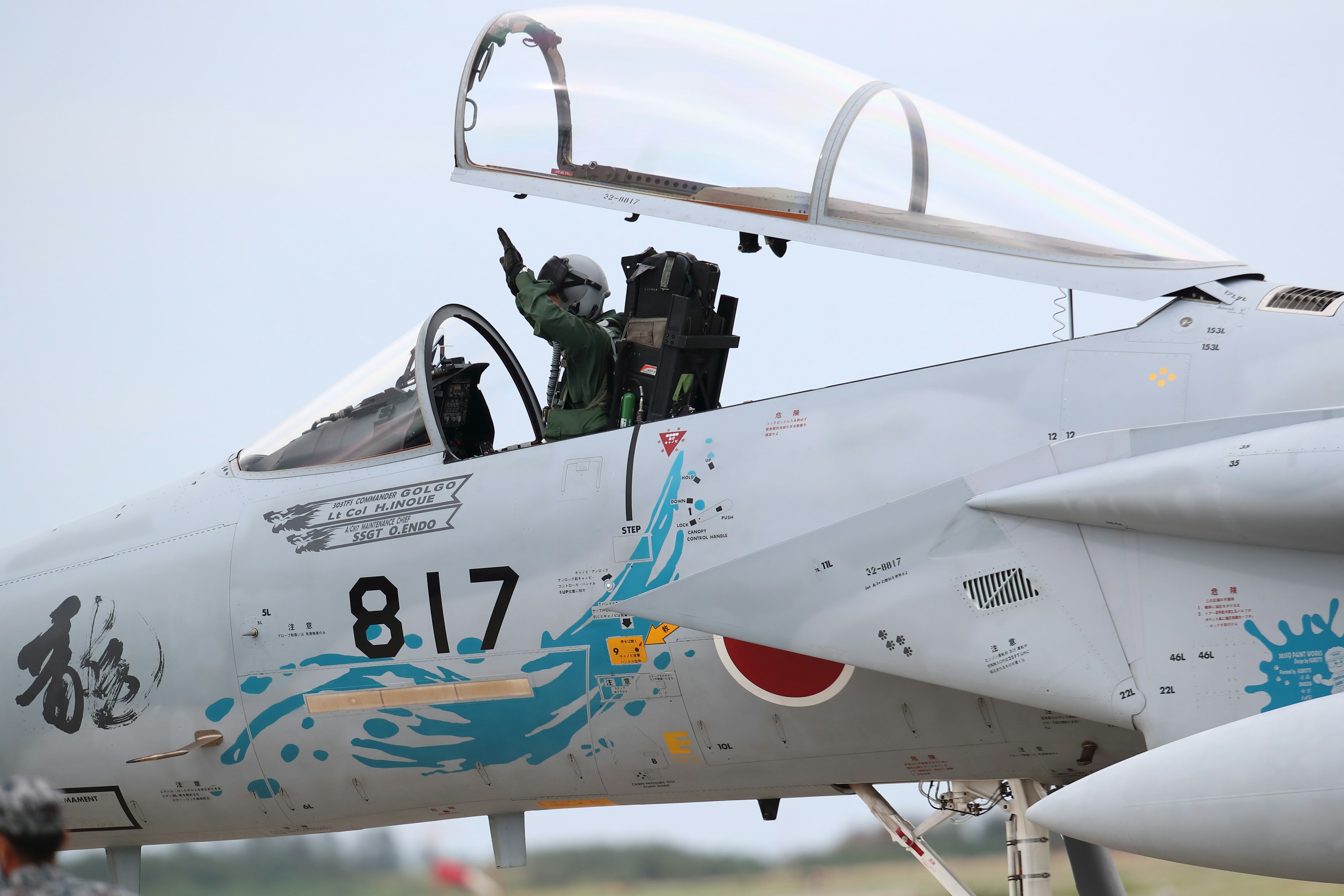 Pilote saluant depuis le cockpit d'un avion de chasse avec des marques colorées