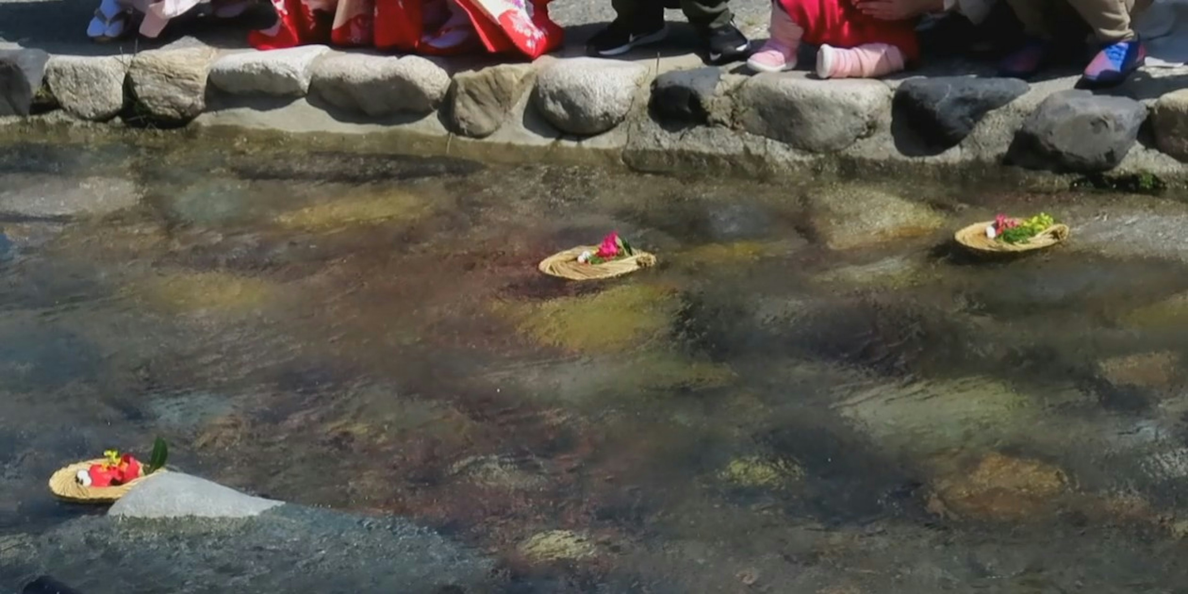 Perahu kecil dekoratif dengan bunga mengapung di atas air dengan orang-orang di dekatnya