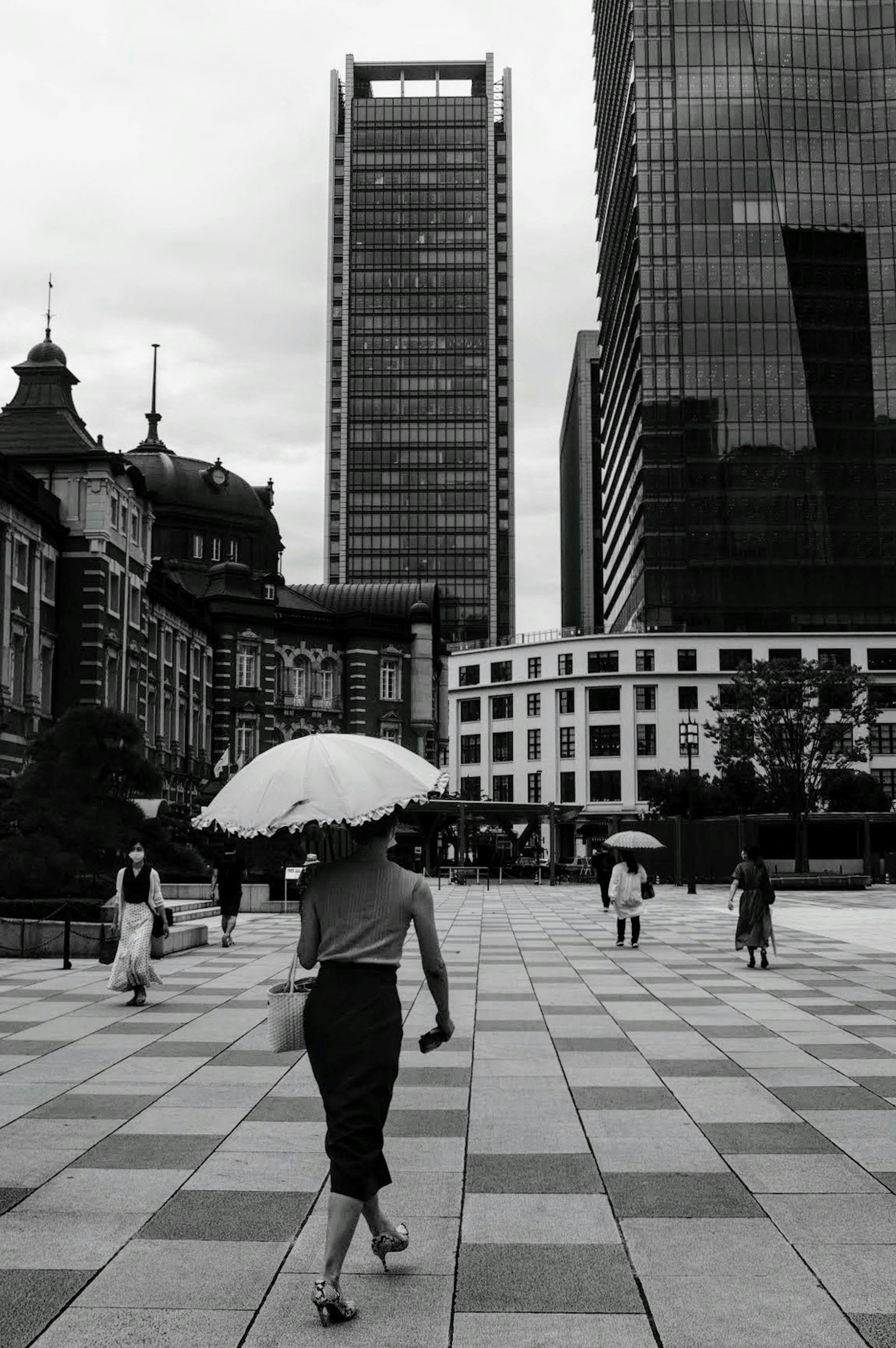 A woman walking with an umbrella in a city square surrounded by modern skyscrapers