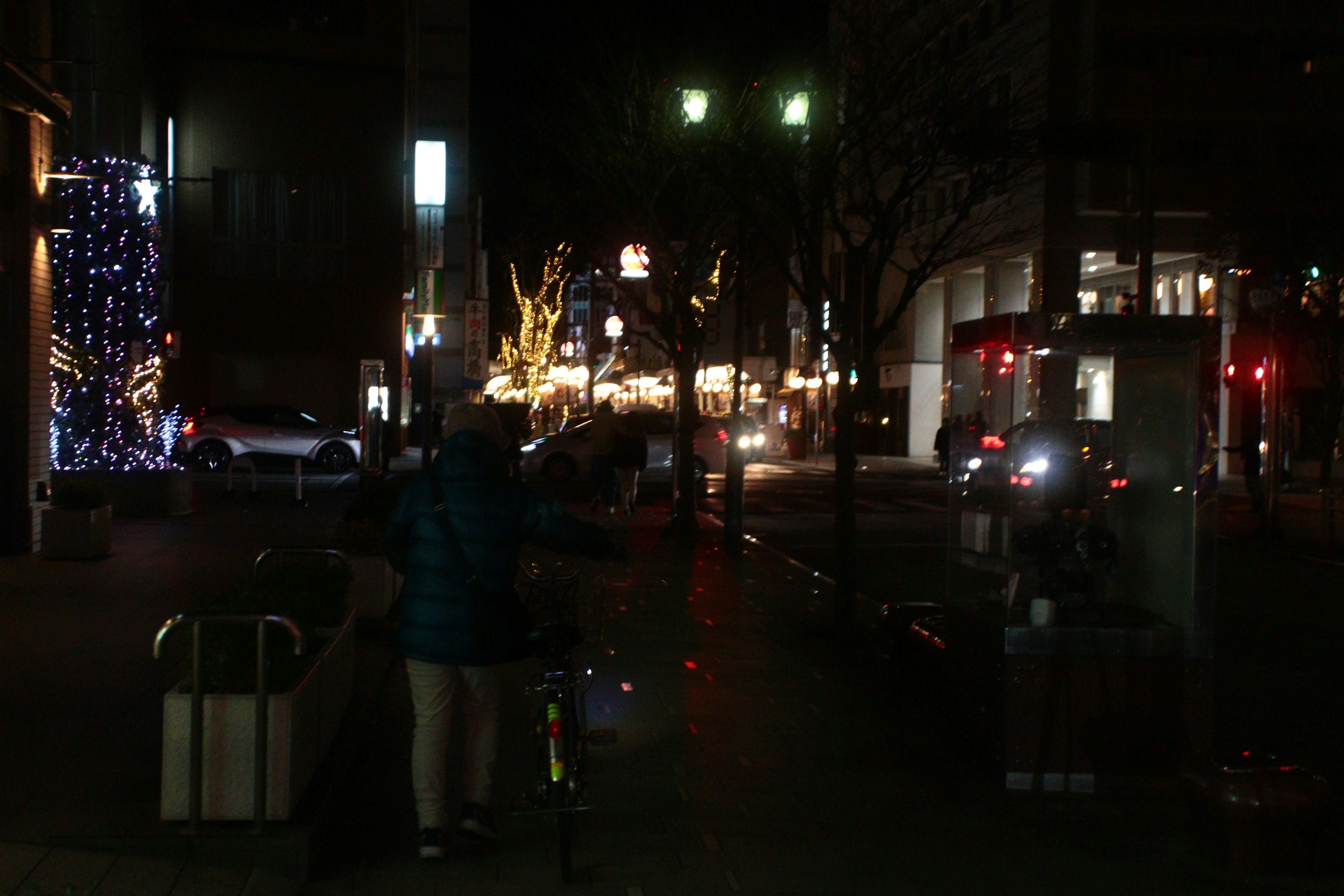 Scène nocturne avec des bâtiments illuminés et une personne poussant un vélo