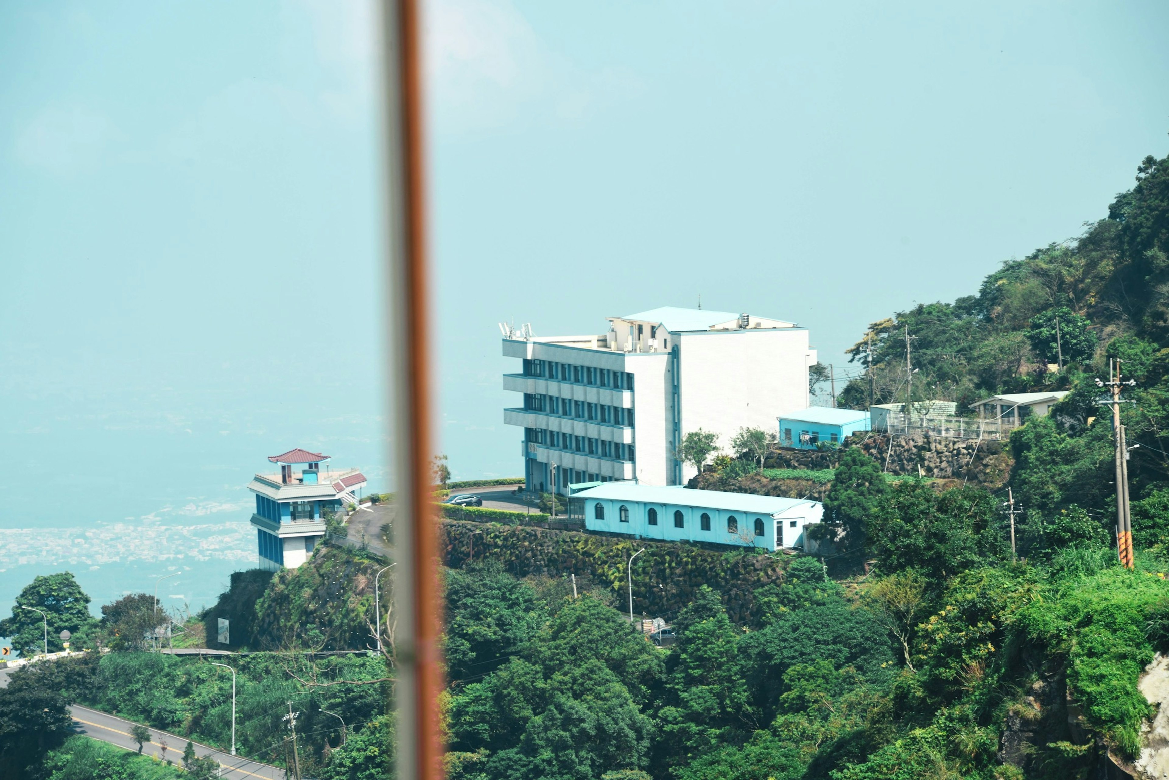 A hillside view featuring blue buildings surrounded by lush greenery