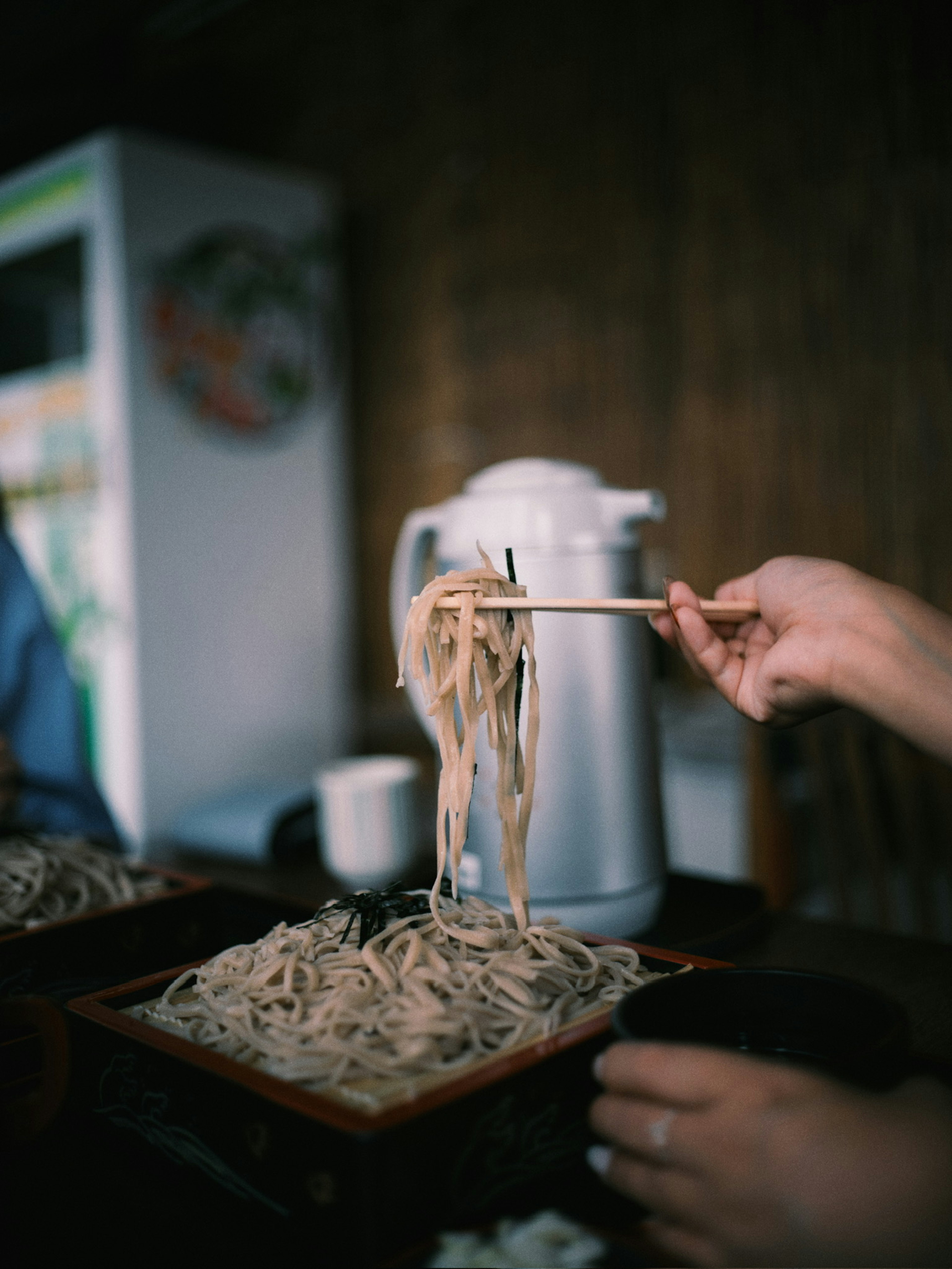 Seseorang menggunakan sumpit untuk mengangkat mie soba dari mangkuk