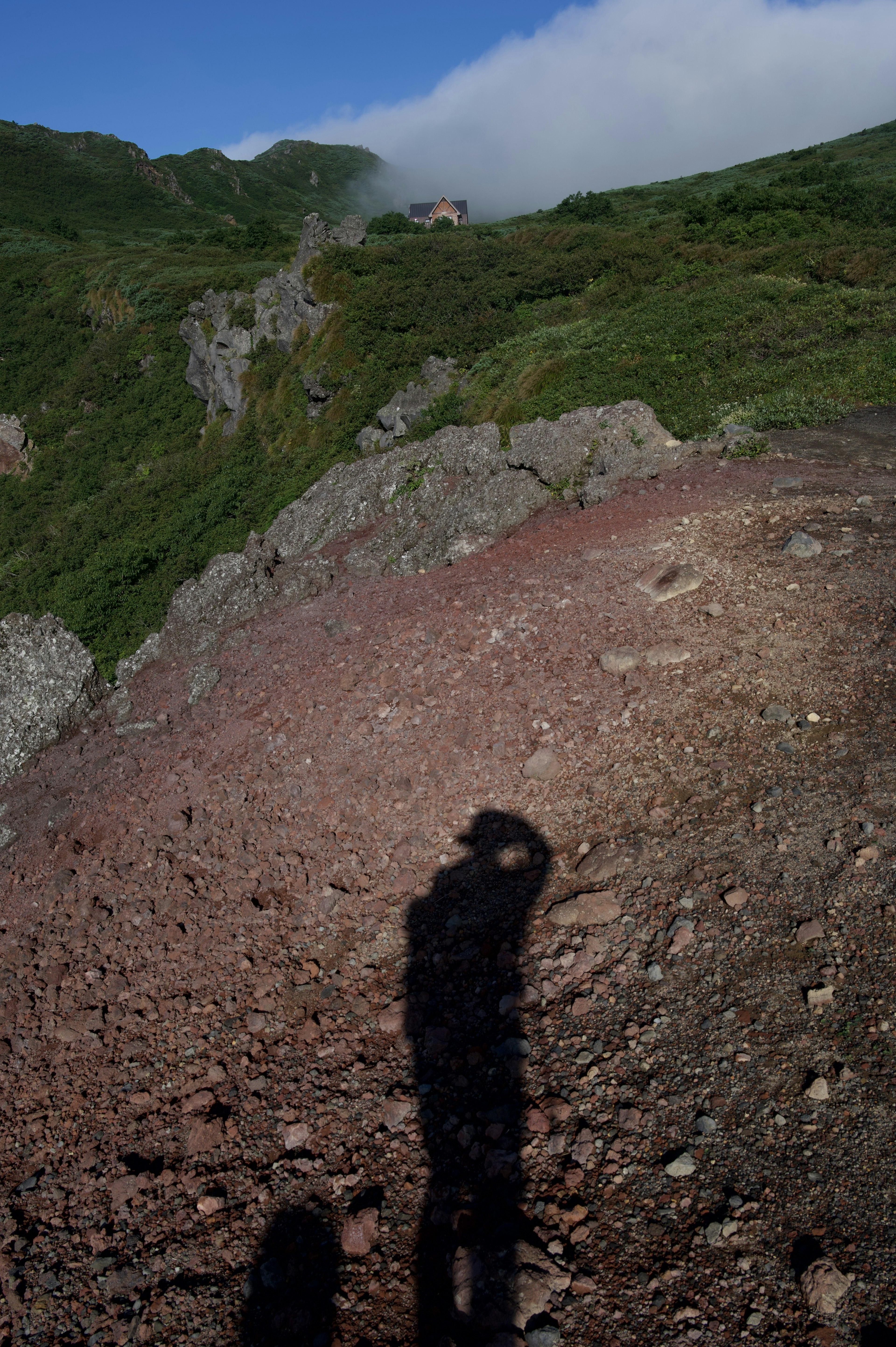 Shadow of a person on rocky terrain with green hills in the background