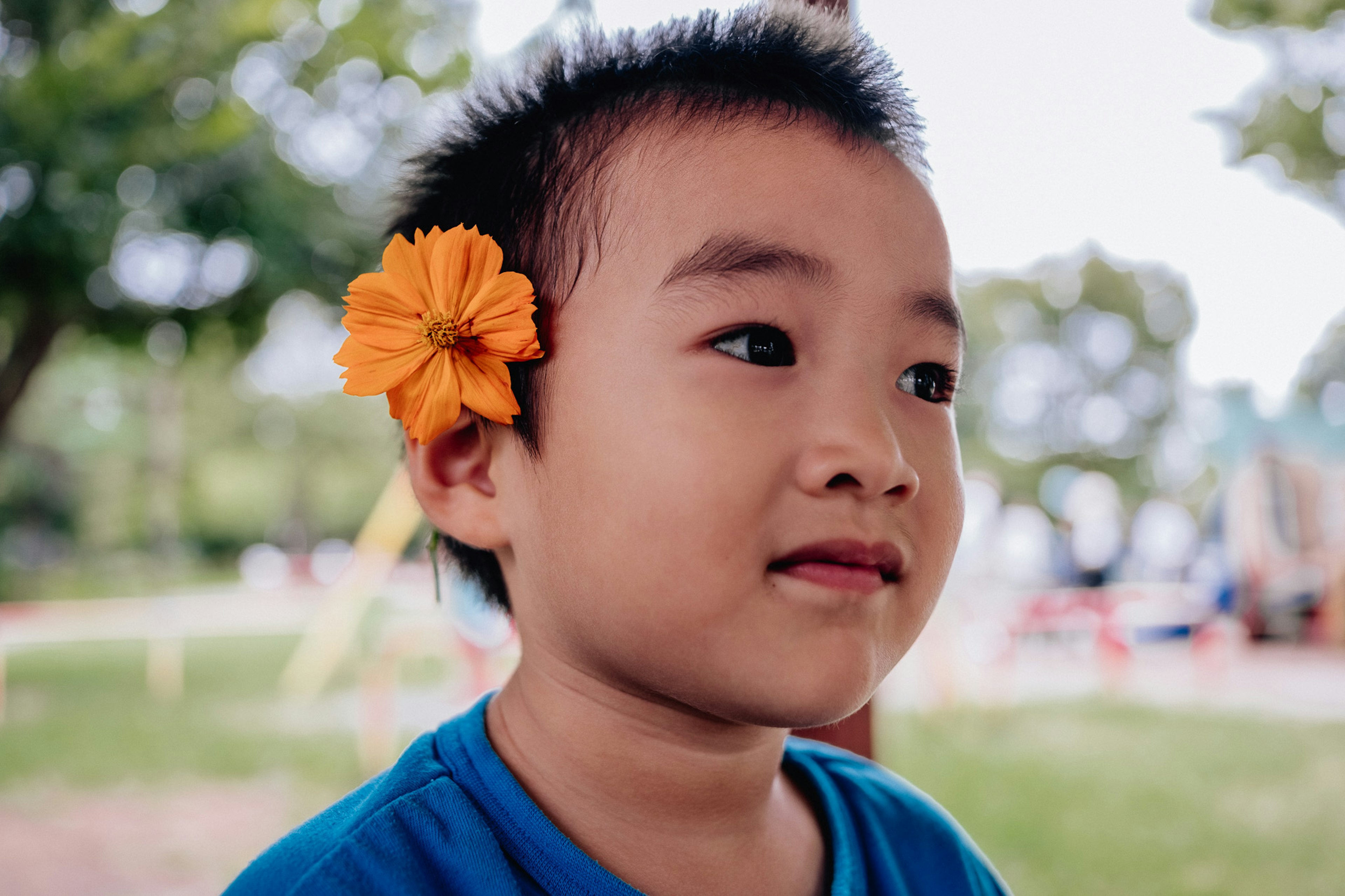 青いシャツを着た少年がオレンジ色の花を耳に挿している