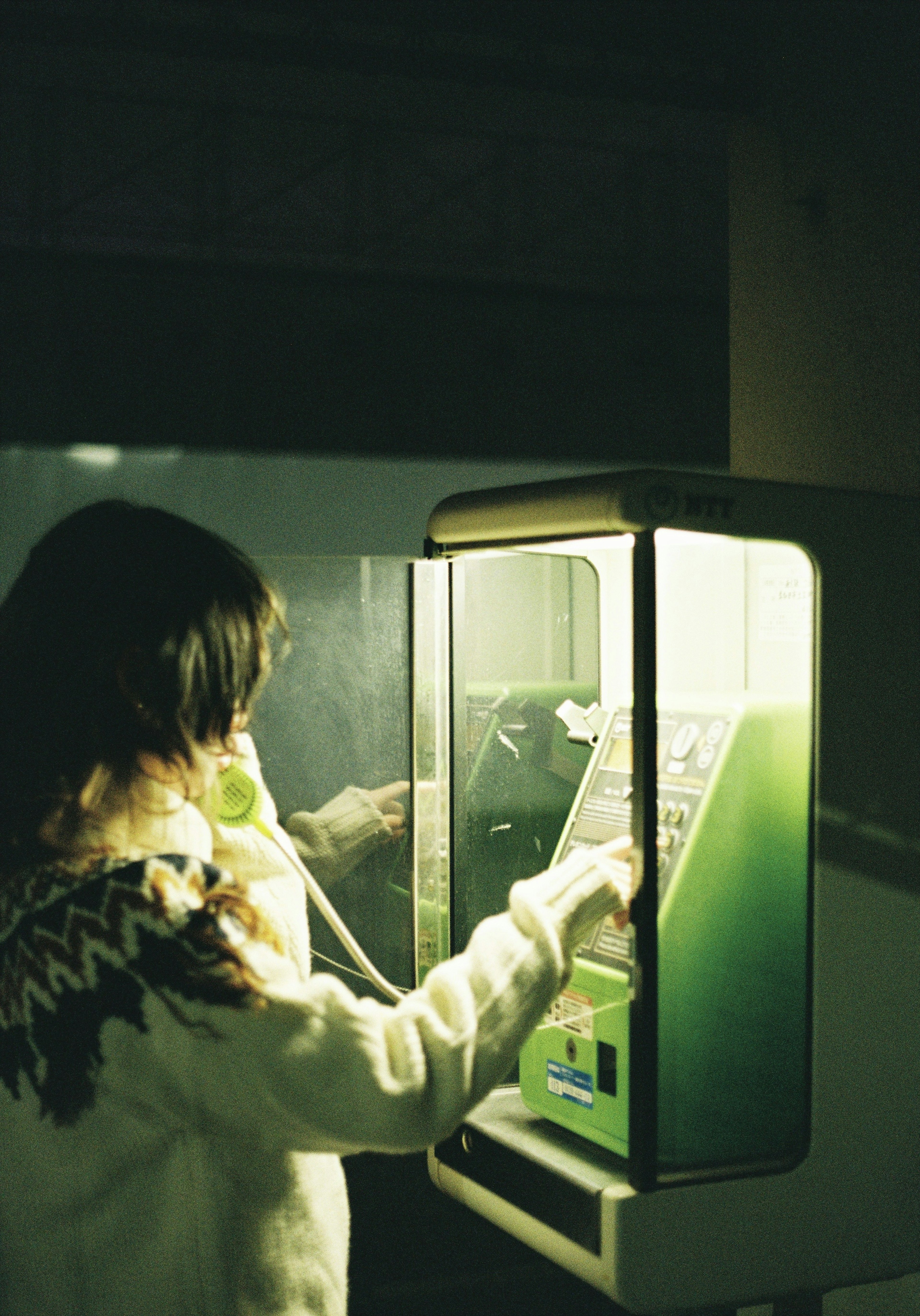 Femme utilisant une cabine téléphonique avec lumière verte, ambiance rétro