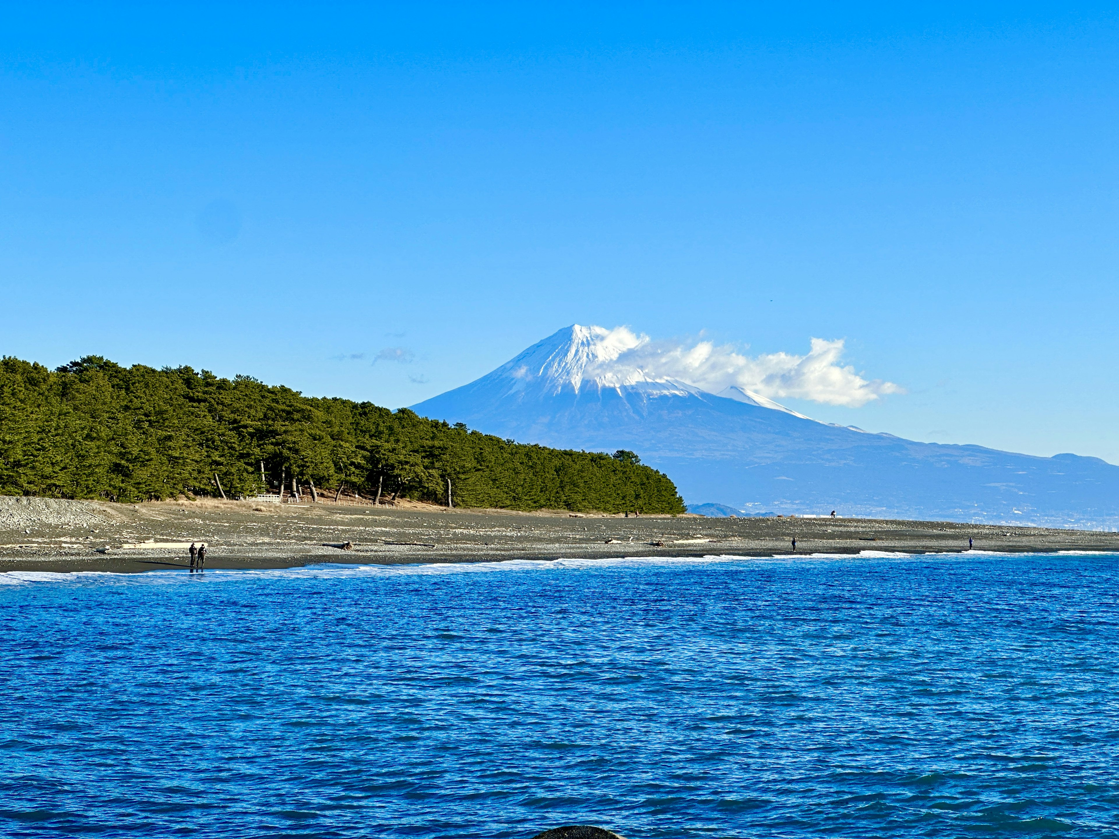 Gunung bersalju di bawah langit biru cerah dengan pemandangan laut yang tenang