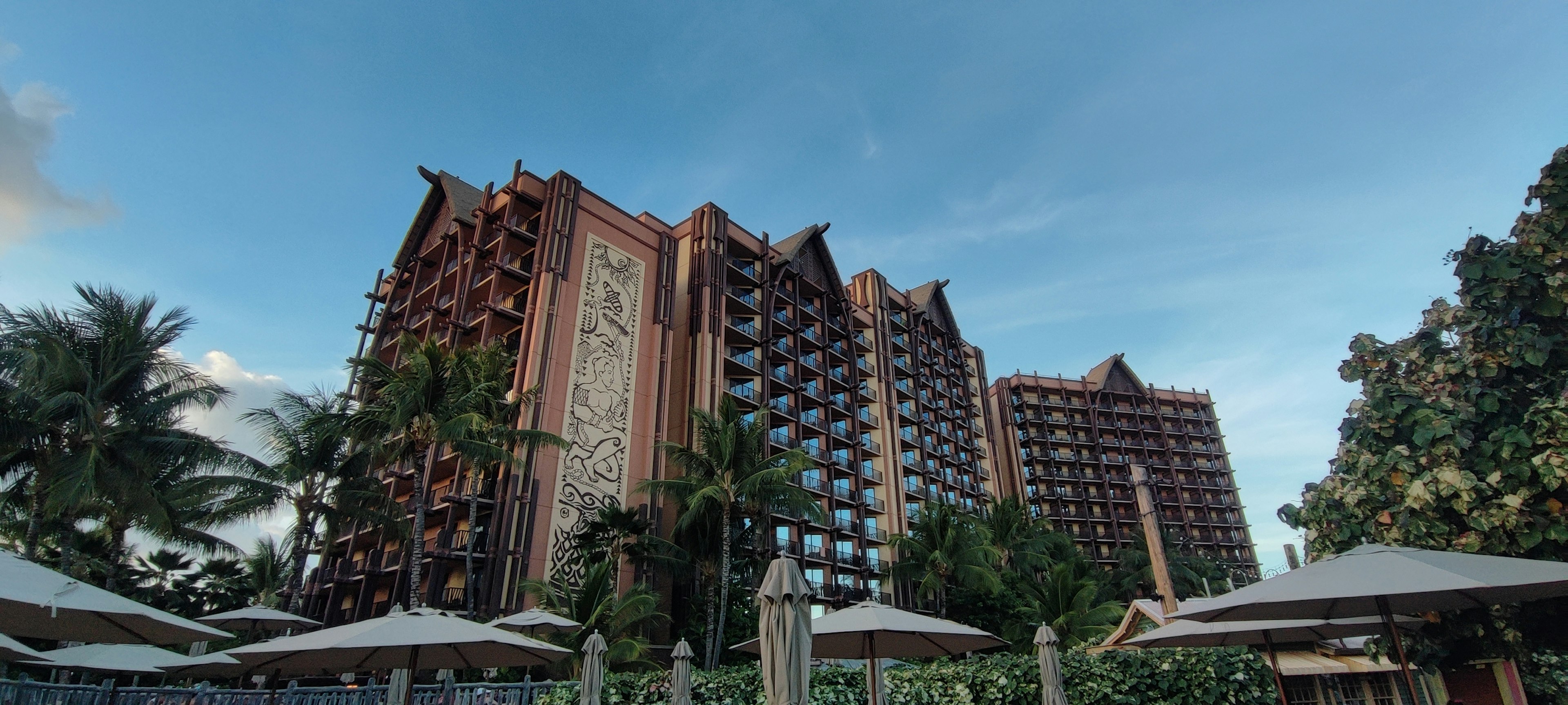 Extérieur d'un hôtel de villégiature avec ciel bleu palmiers et parasols