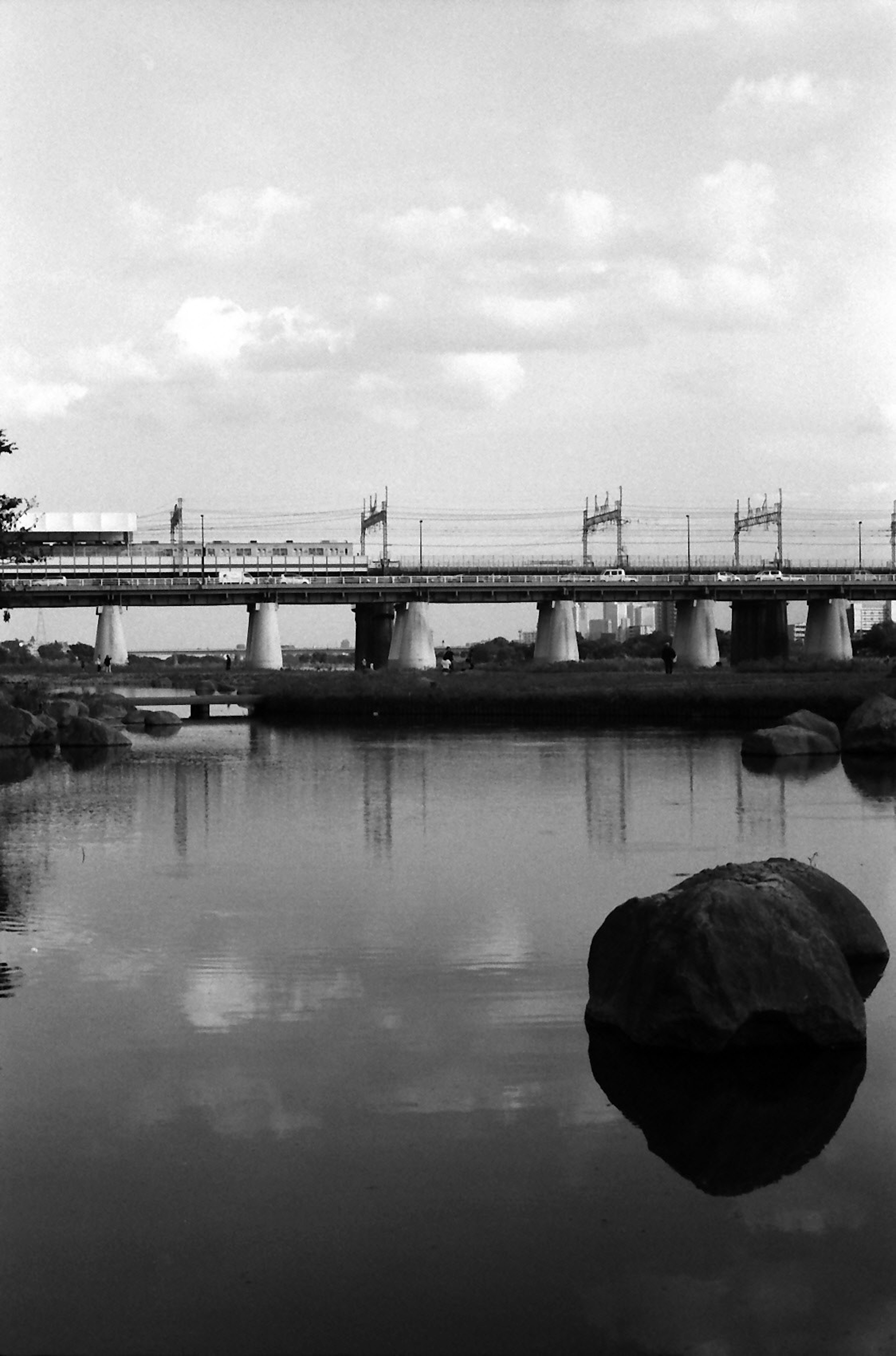 Schwarz-weiß Landschaft mit einer Brücke und einem Stein, der sich im ruhigen Wasser spiegelt