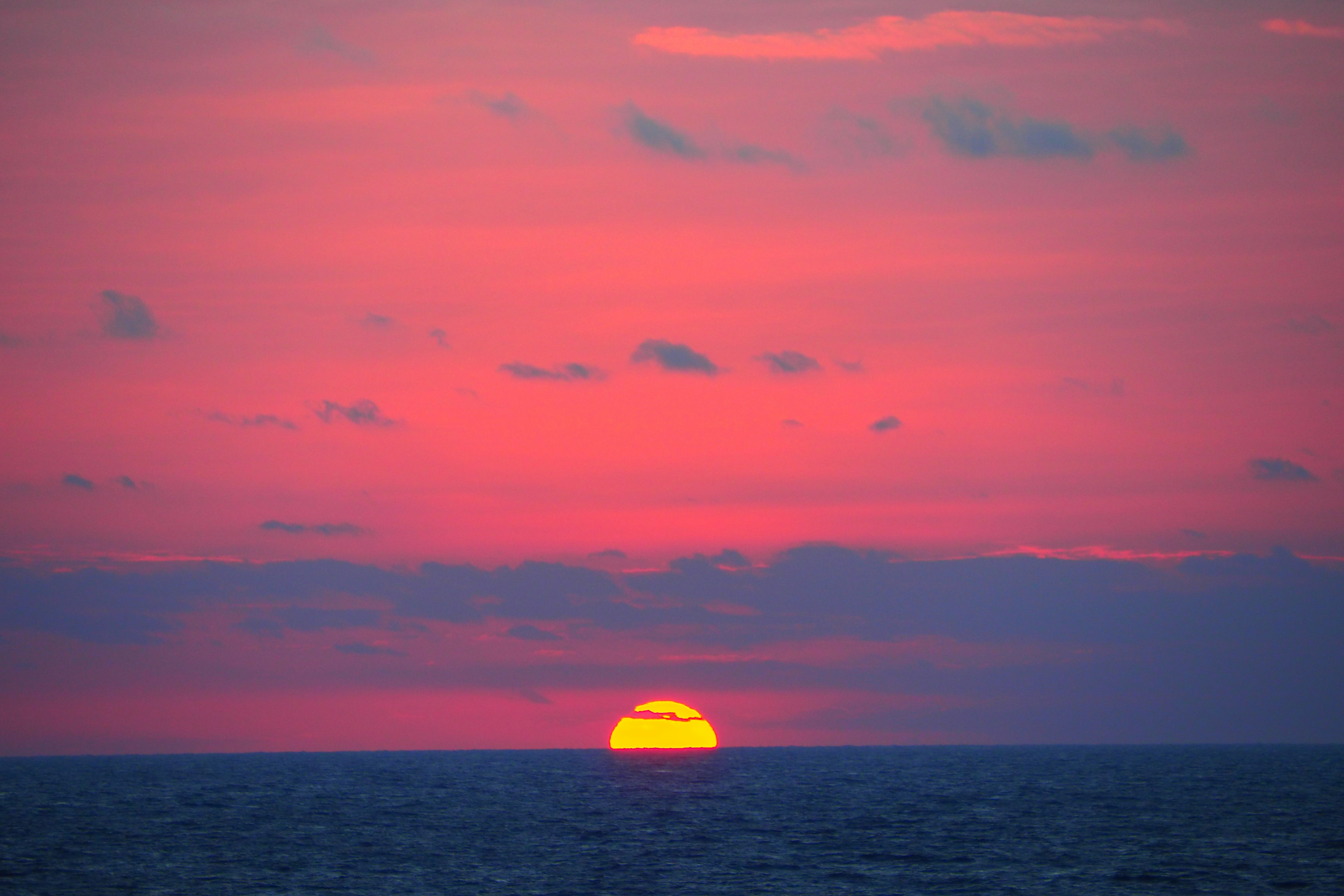 海の水平線に沈む太陽とピンクの空