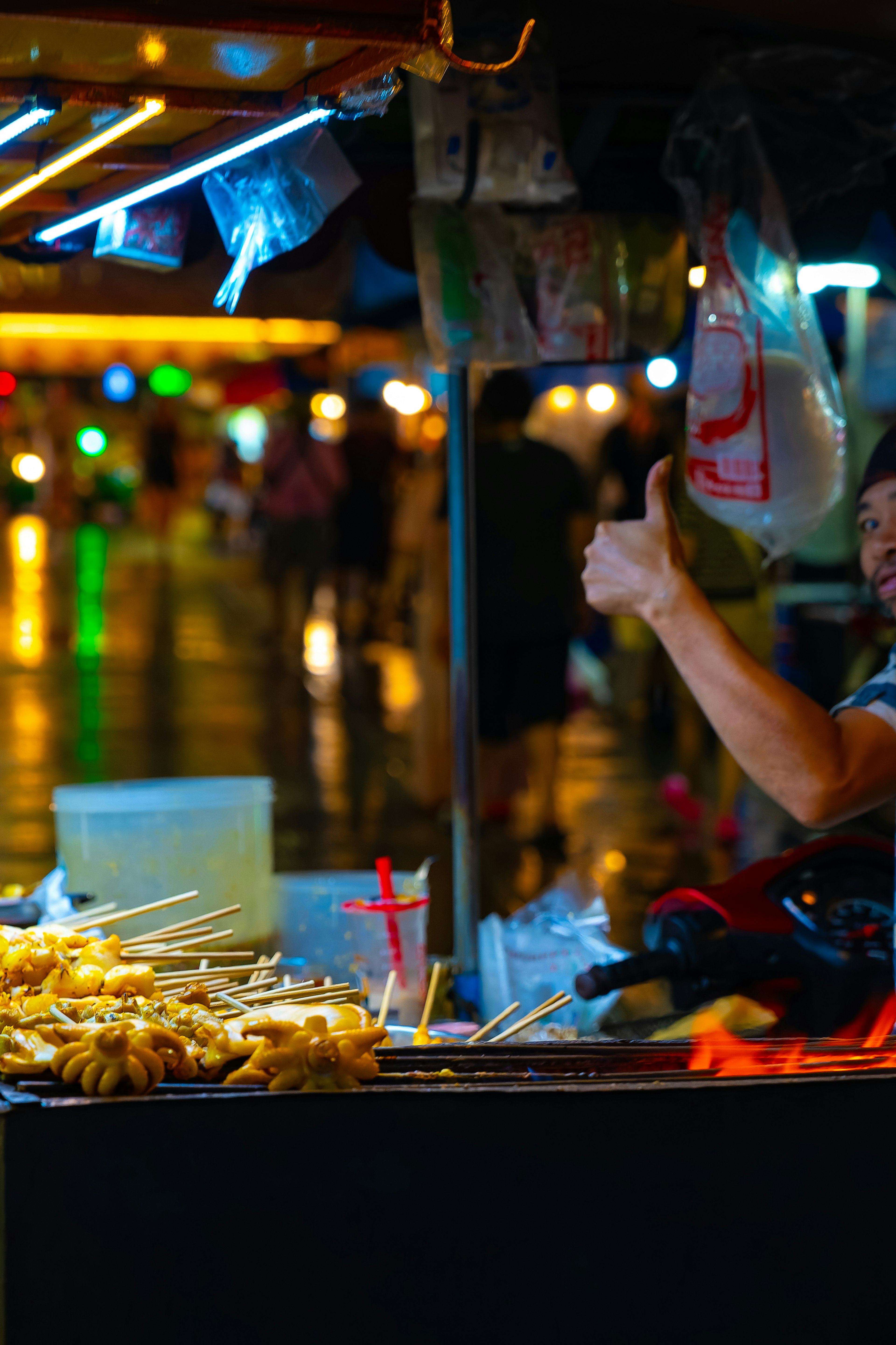 Un venditore di strada che fa un pollice in su mentre vende snack di notte