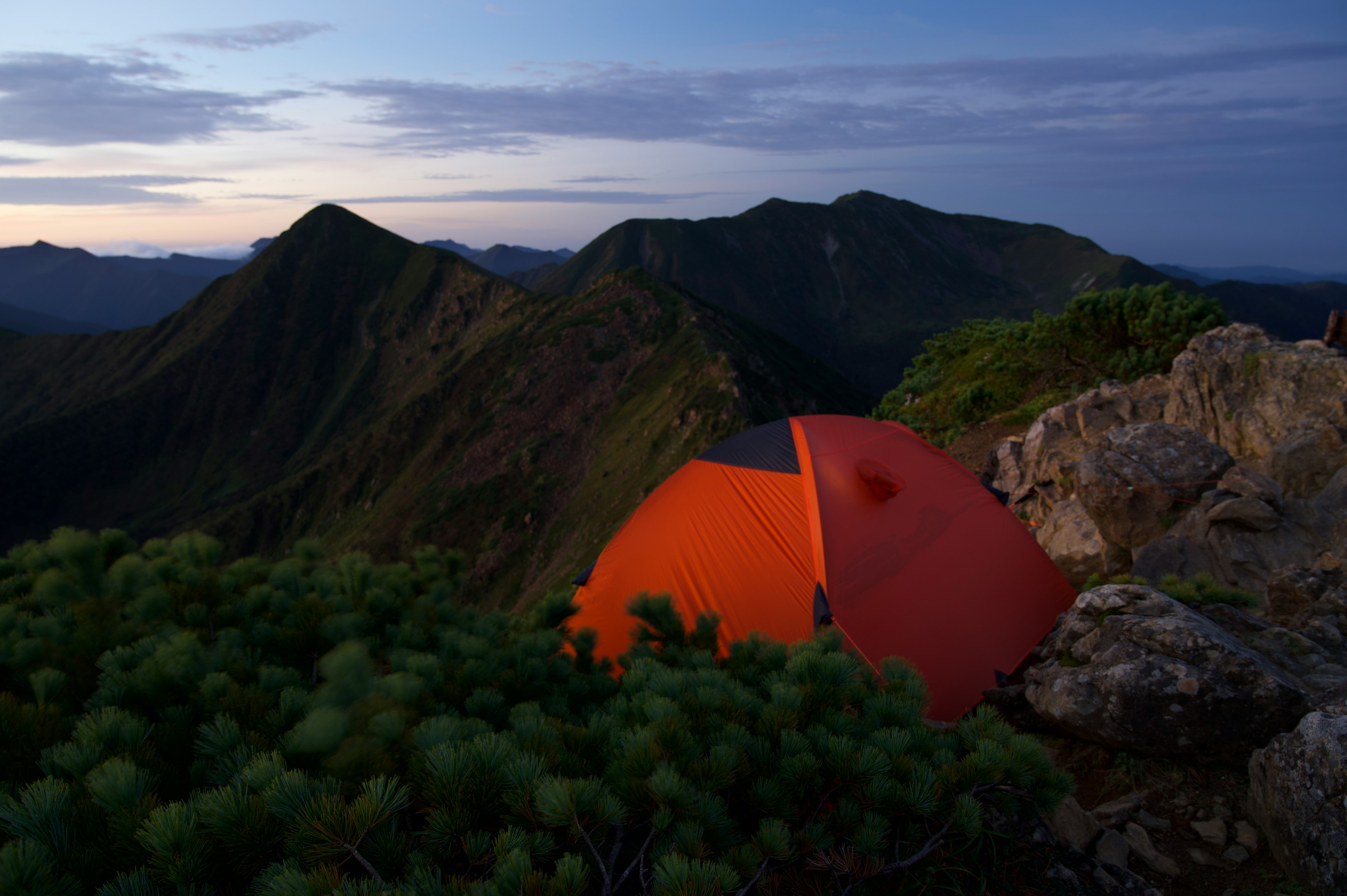 夕暮れの山の風景にオレンジ色のテントが見える