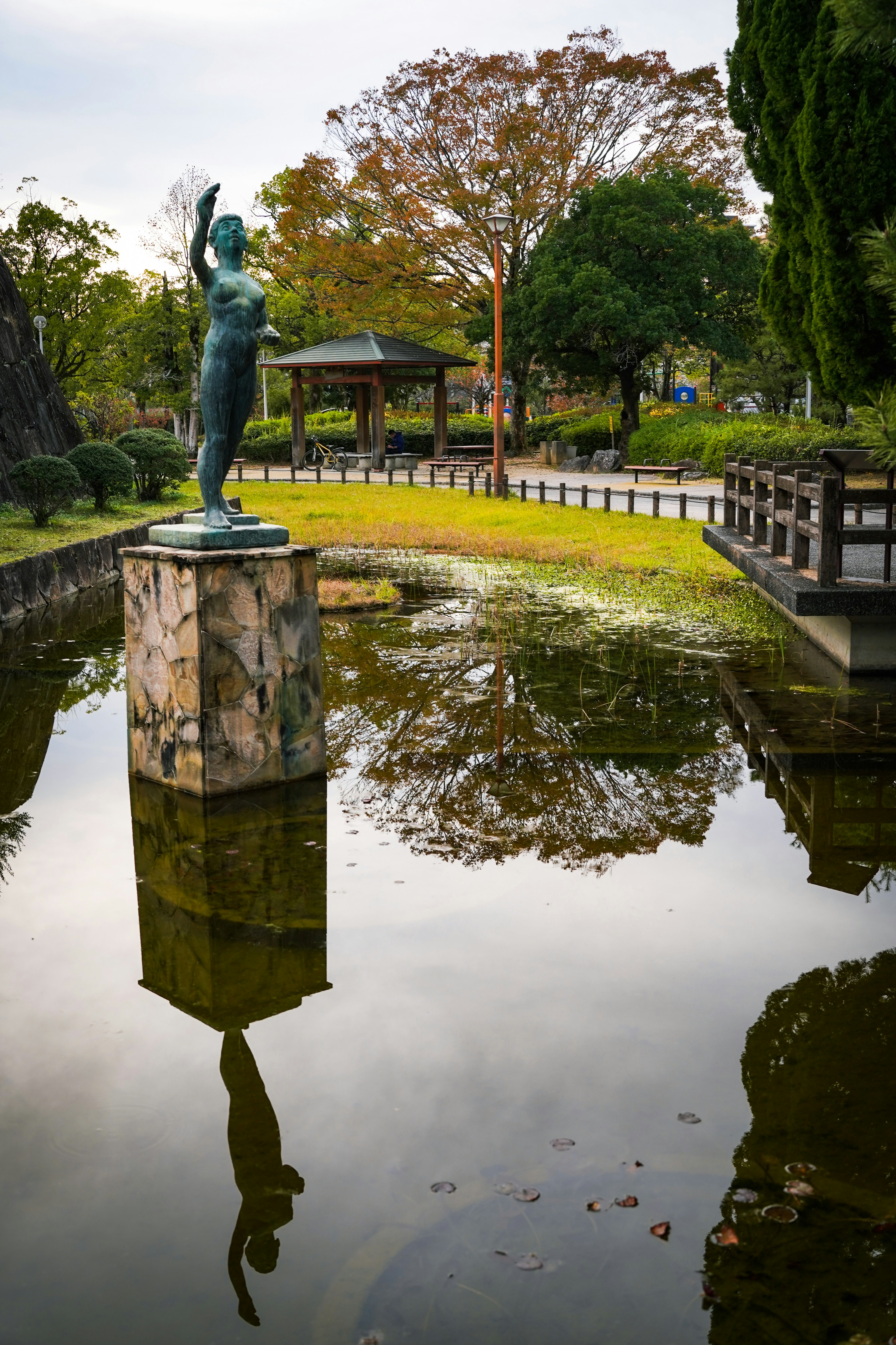 公園の池に立つ像の反射と周囲の緑