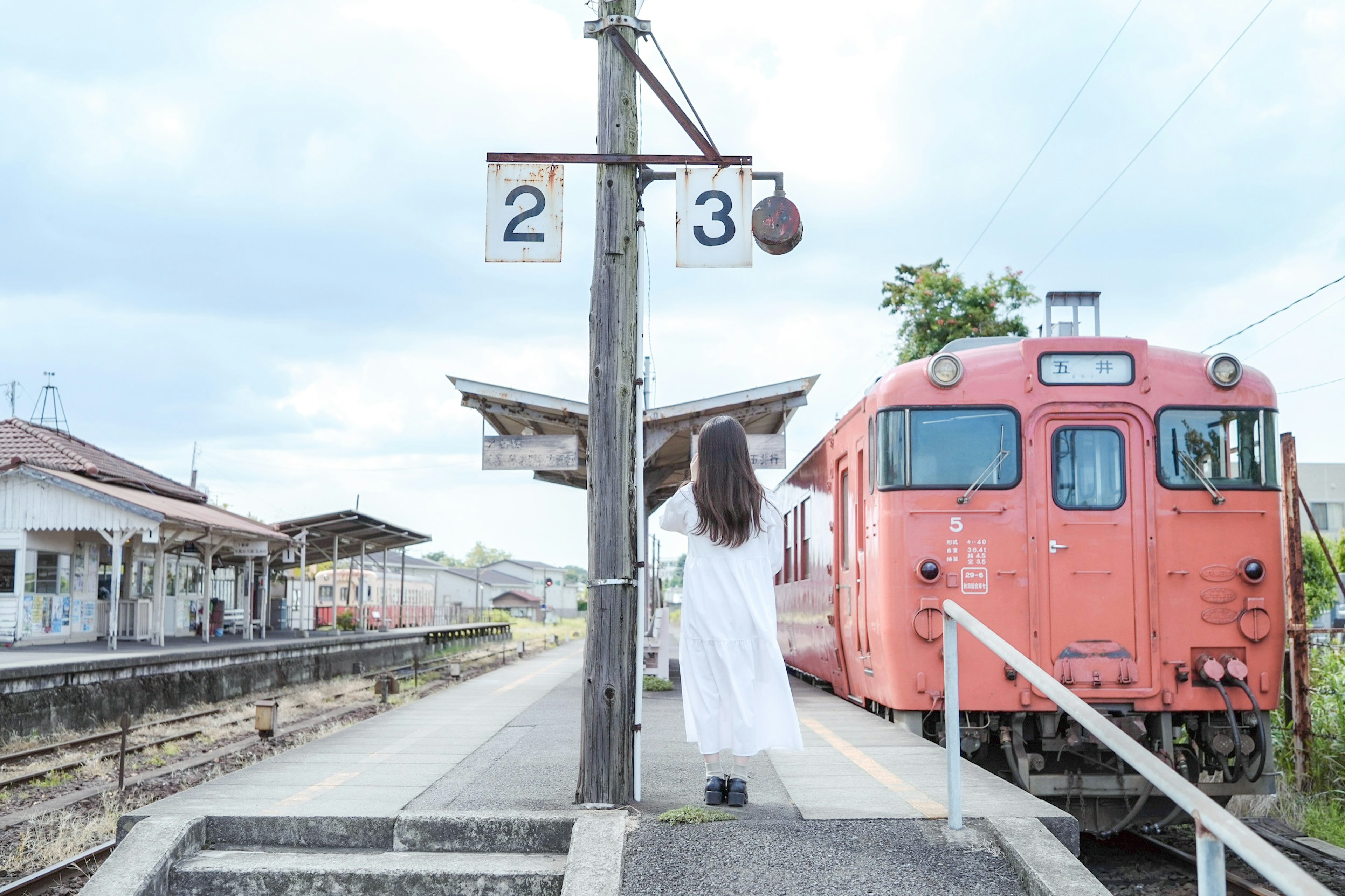 A woman in white standing at a train station with a red train