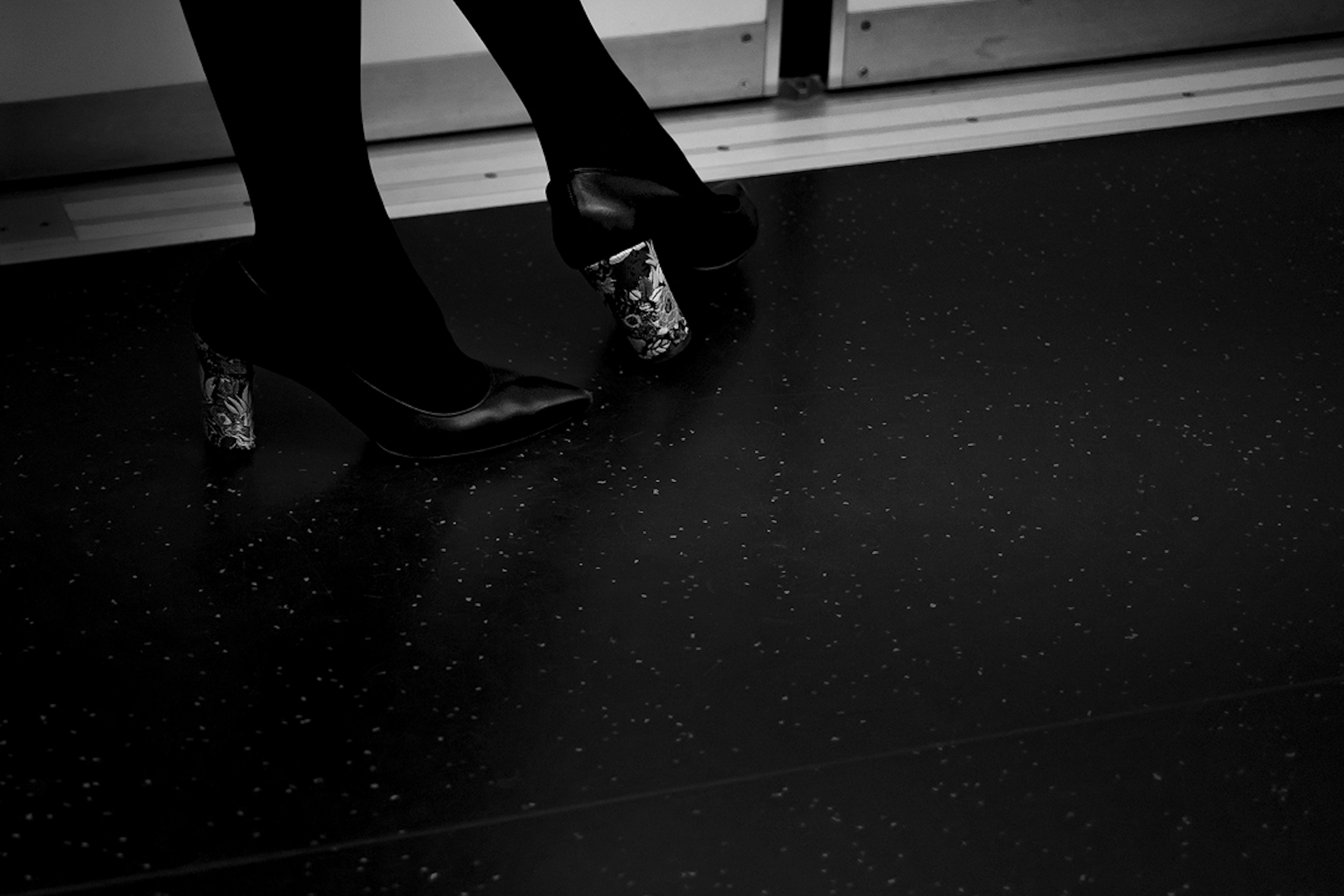 Close-up of a woman’s feet in black heels on a dark floor