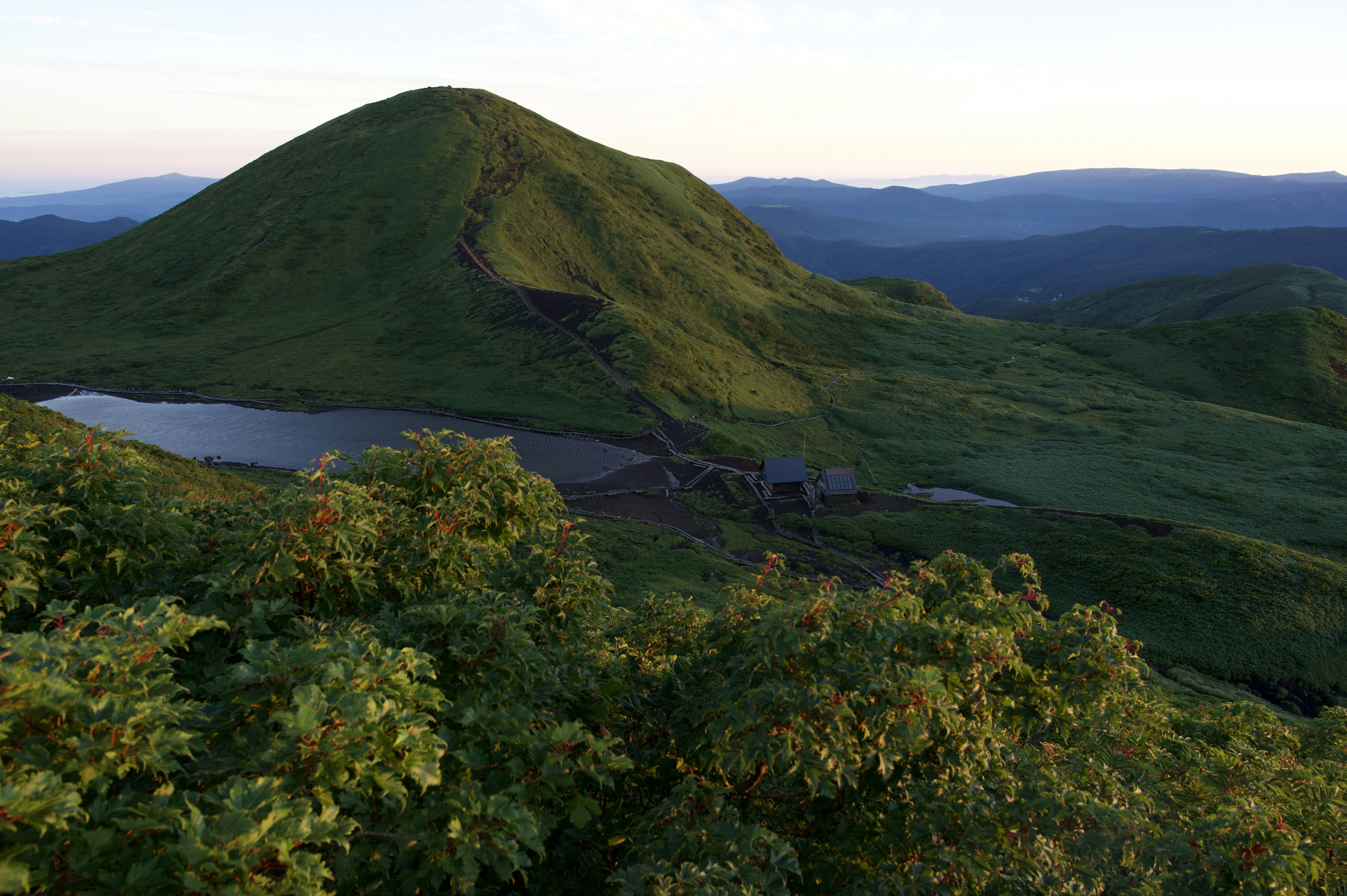 Vista escénica de colinas verdes y un lago con montañas a lo lejos