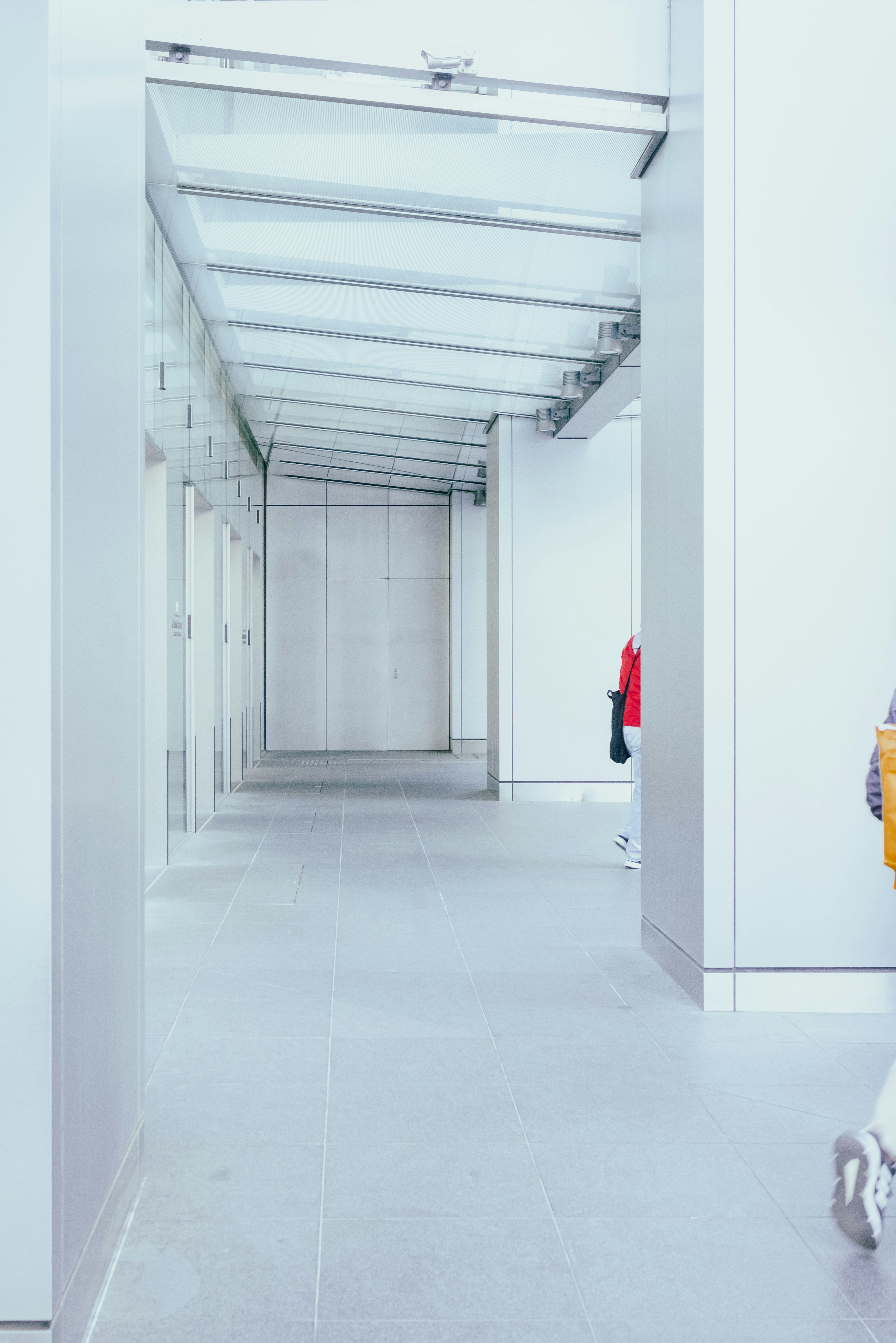 Bright white hallway with a transparent glass roof and a red garment visible in the distance