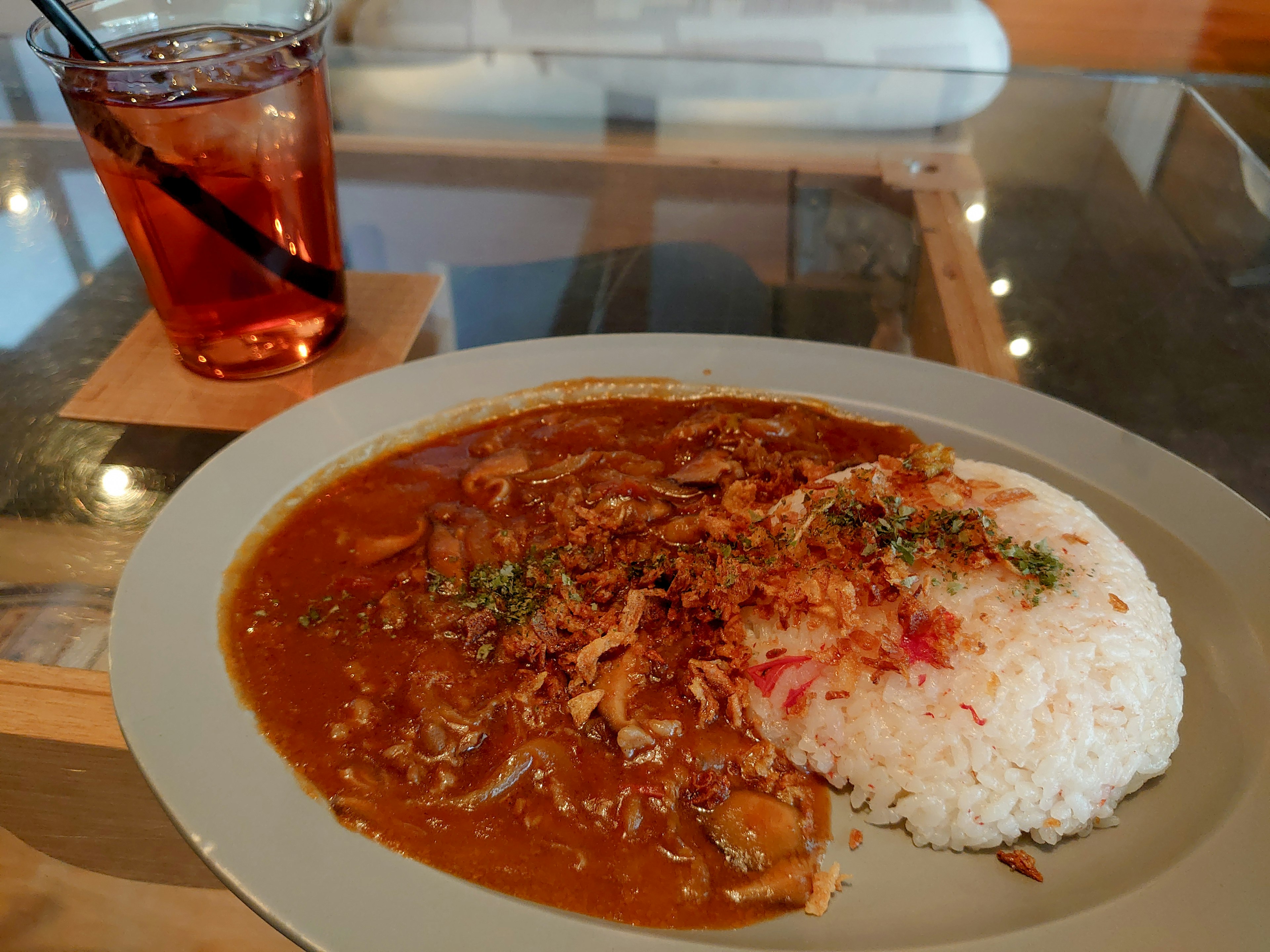 Plate of curry with rice garnished with herbs and fried onions alongside a drink