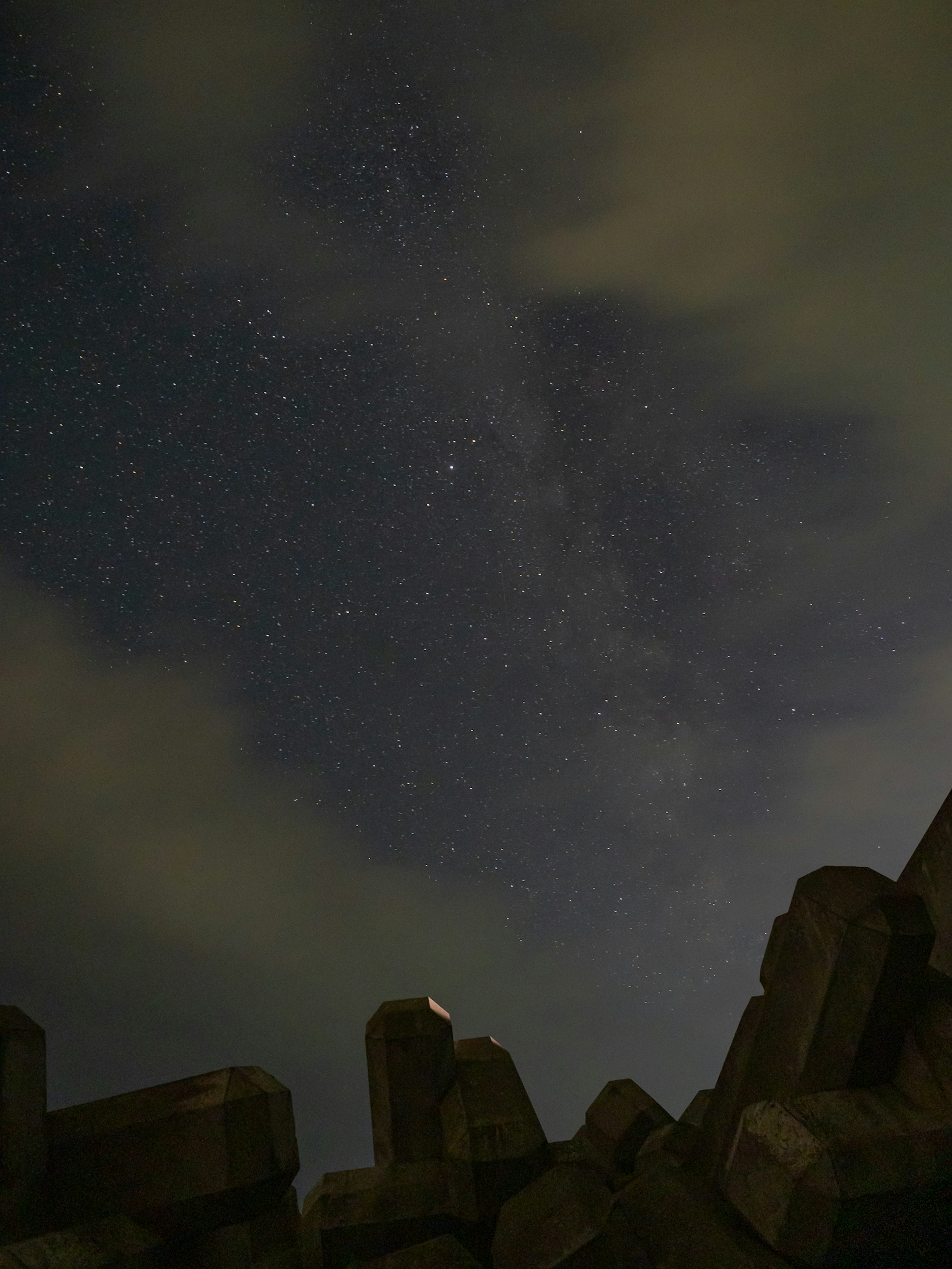 Silhouette of rocks under a starry night sky with faint clouds