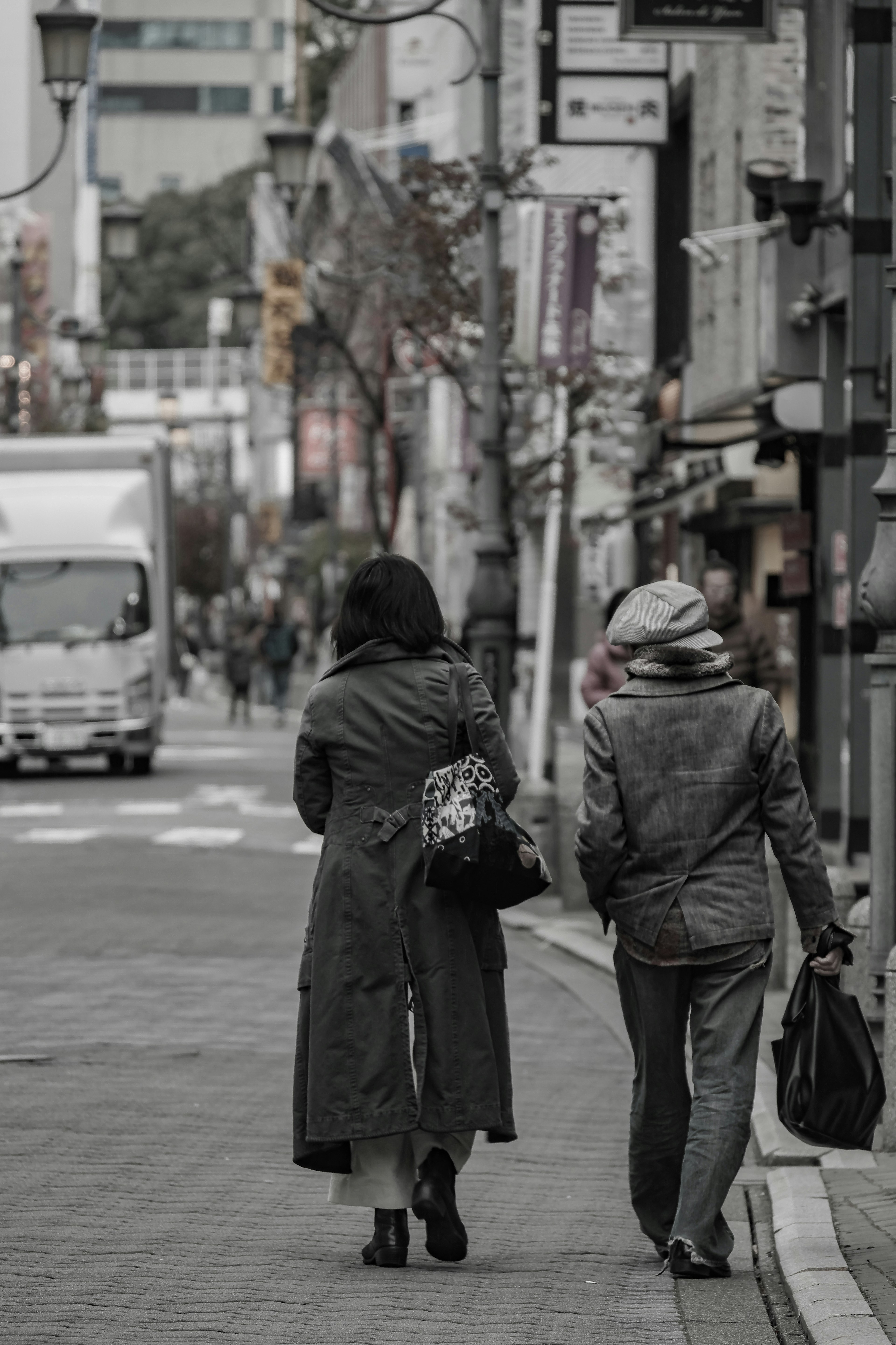 兩位穿著外套的女性走在街上，附近停著一輛卡車