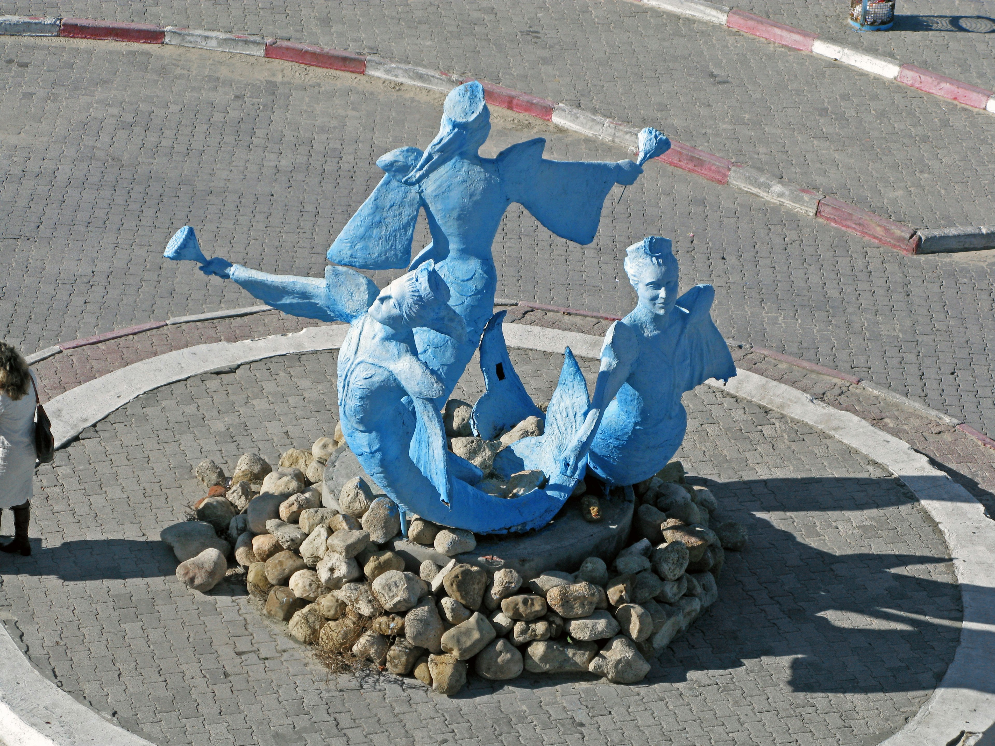 Blaue Fischskulptur in der Mitte, umgeben von Steinen, die Figuren zeigen, die mit Fischen spielen