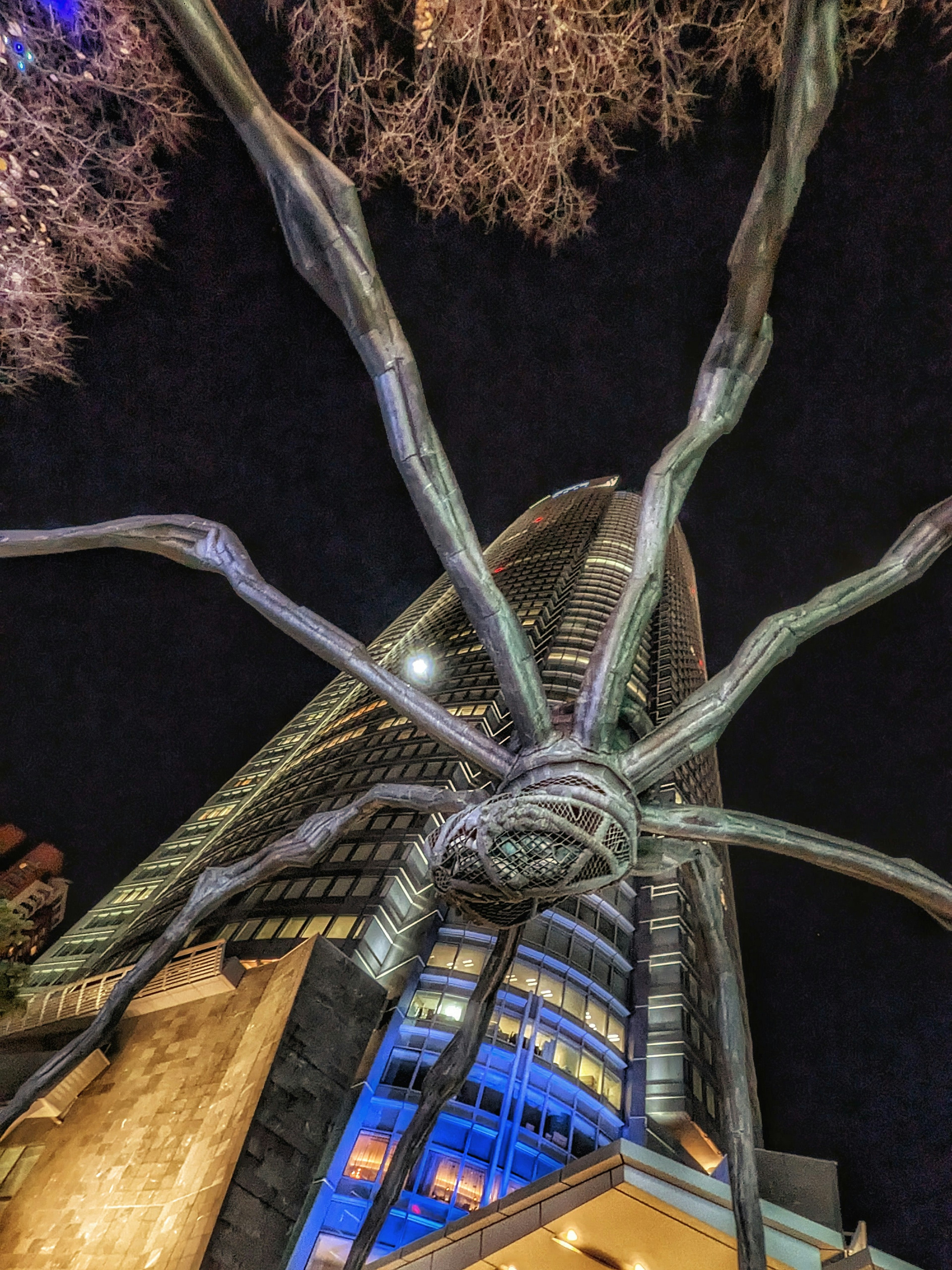 Eine große Spinnen-Skulptur unter dem Nachthimmel, die sich von einem Wolkenkratzer abhebt