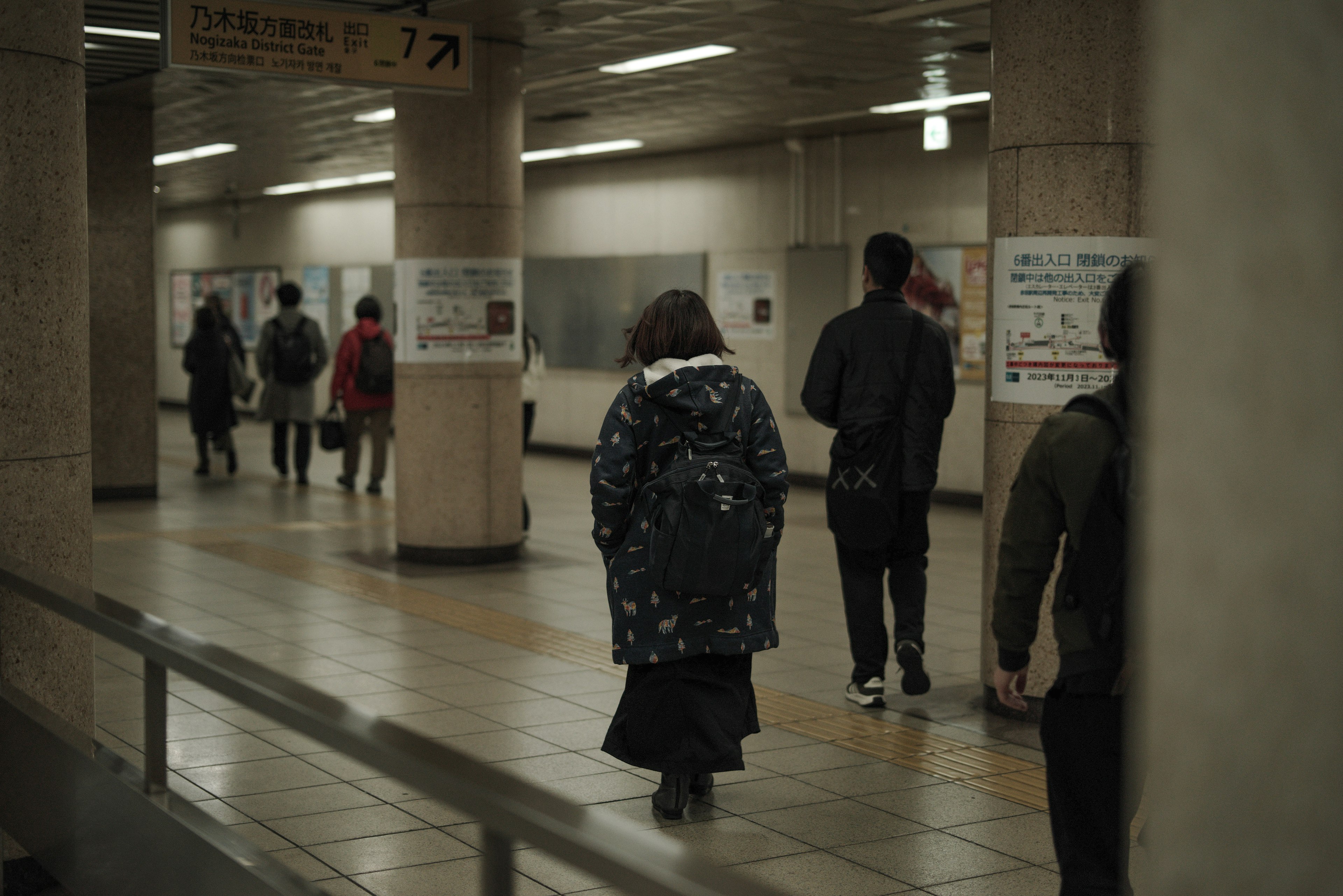 People walking in a subway station with a woman in a patterned coat