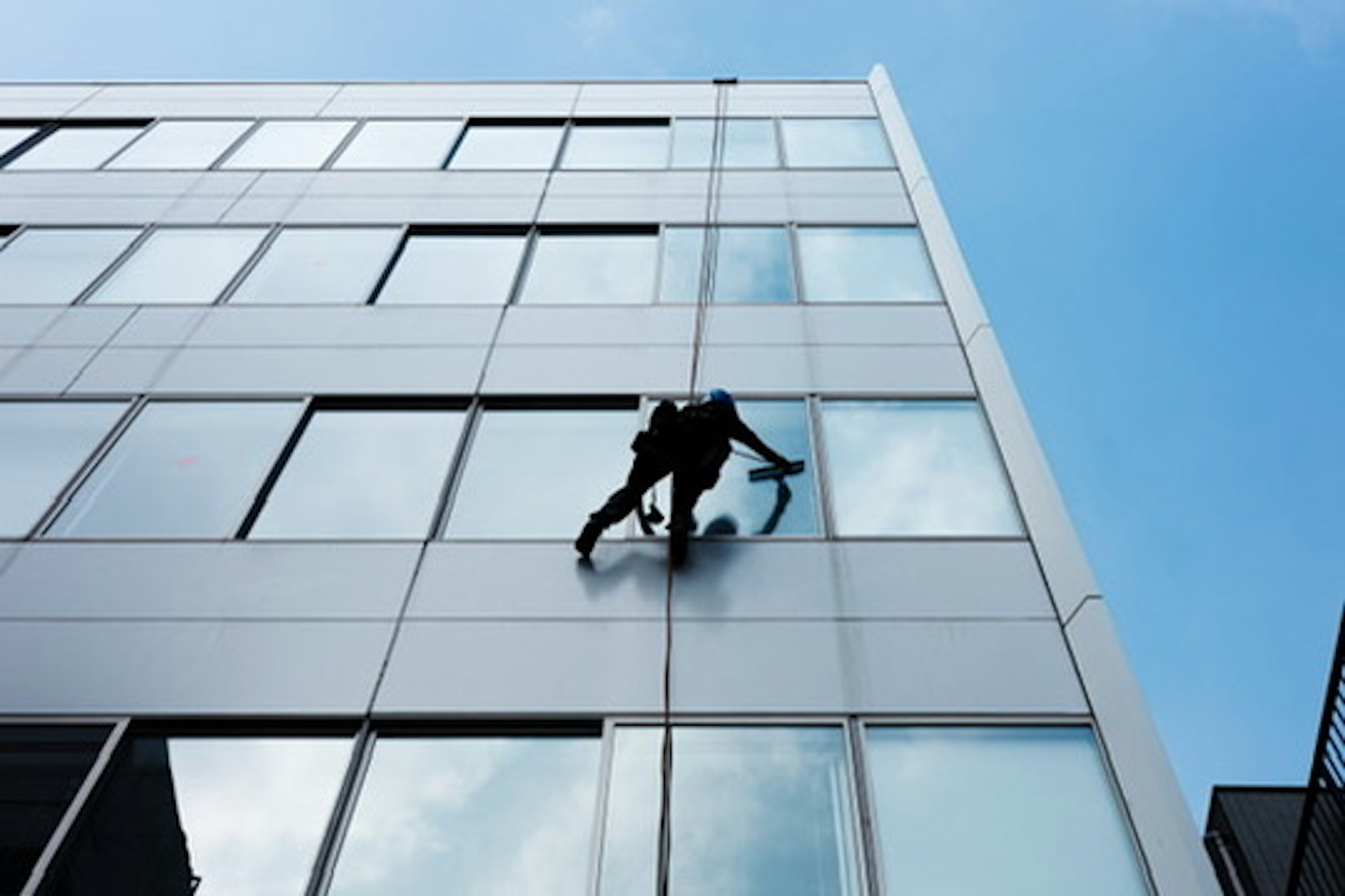 Silhouette eines Arbeiters, der Fenster an einem Gebäude mit blauem Himmel reinigt