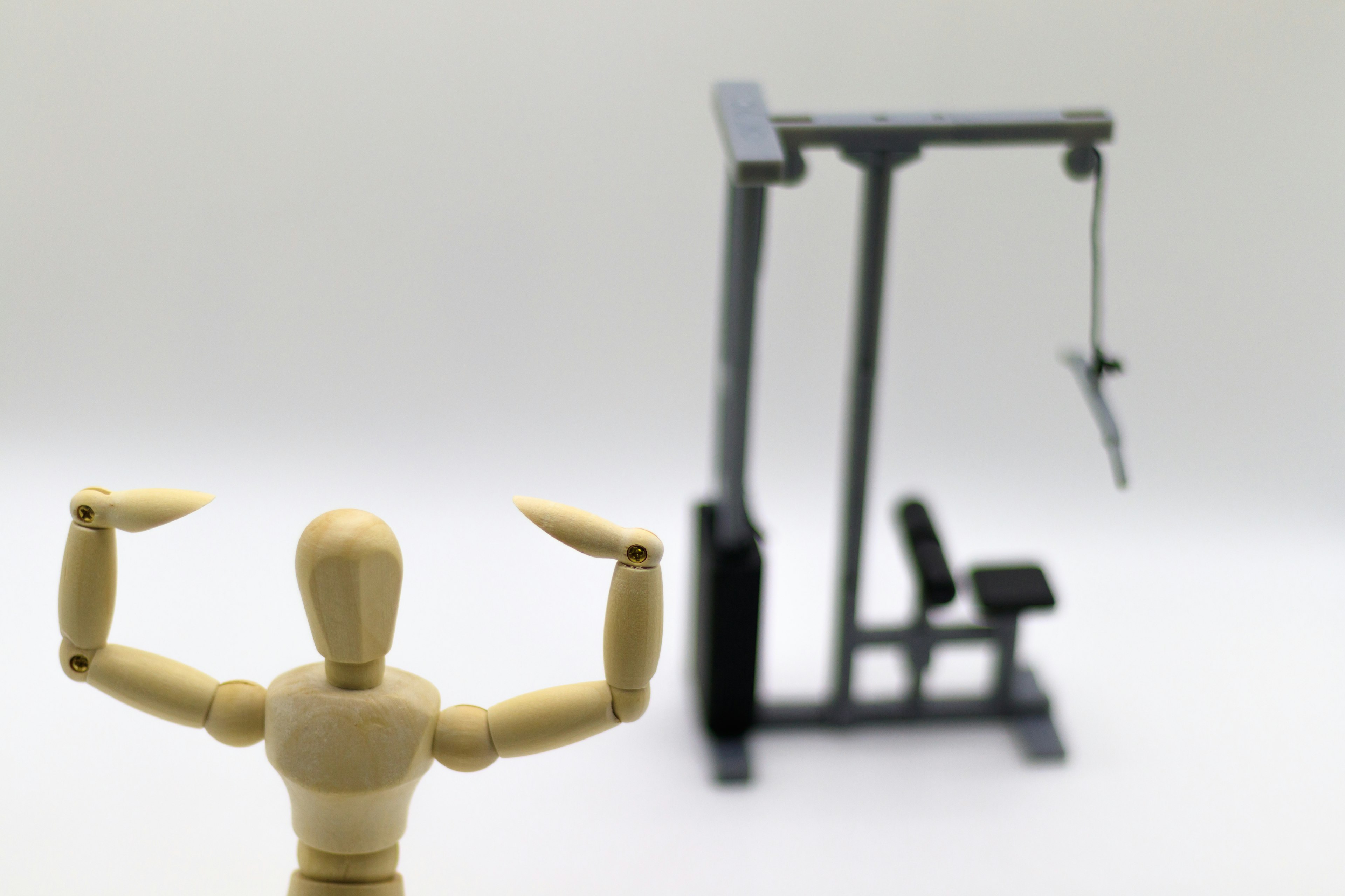 Un maniquí de madera flexionando músculos con equipo de gimnasio al fondo