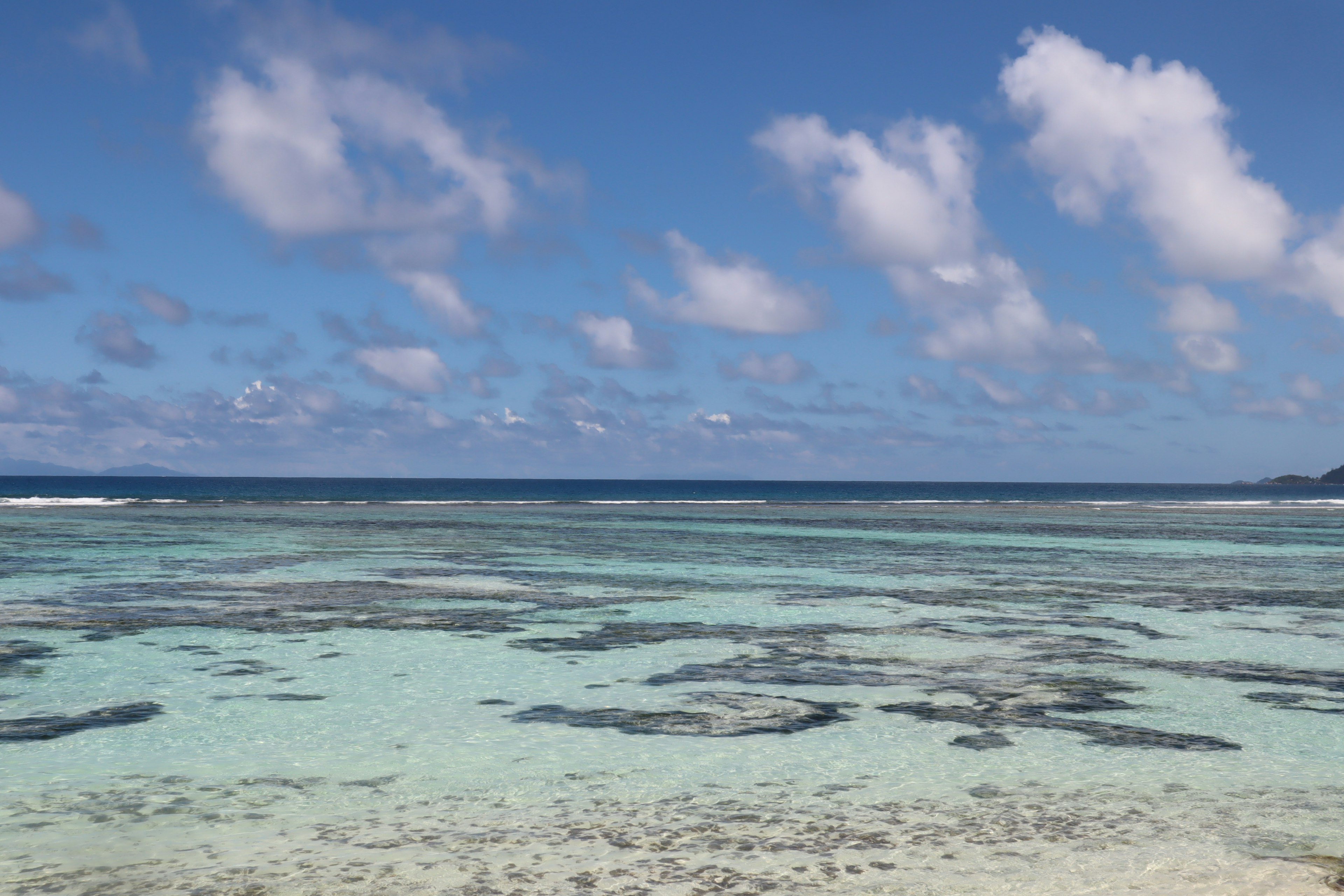 Scenic view of a clear turquoise sea with coral reefs and fluffy clouds