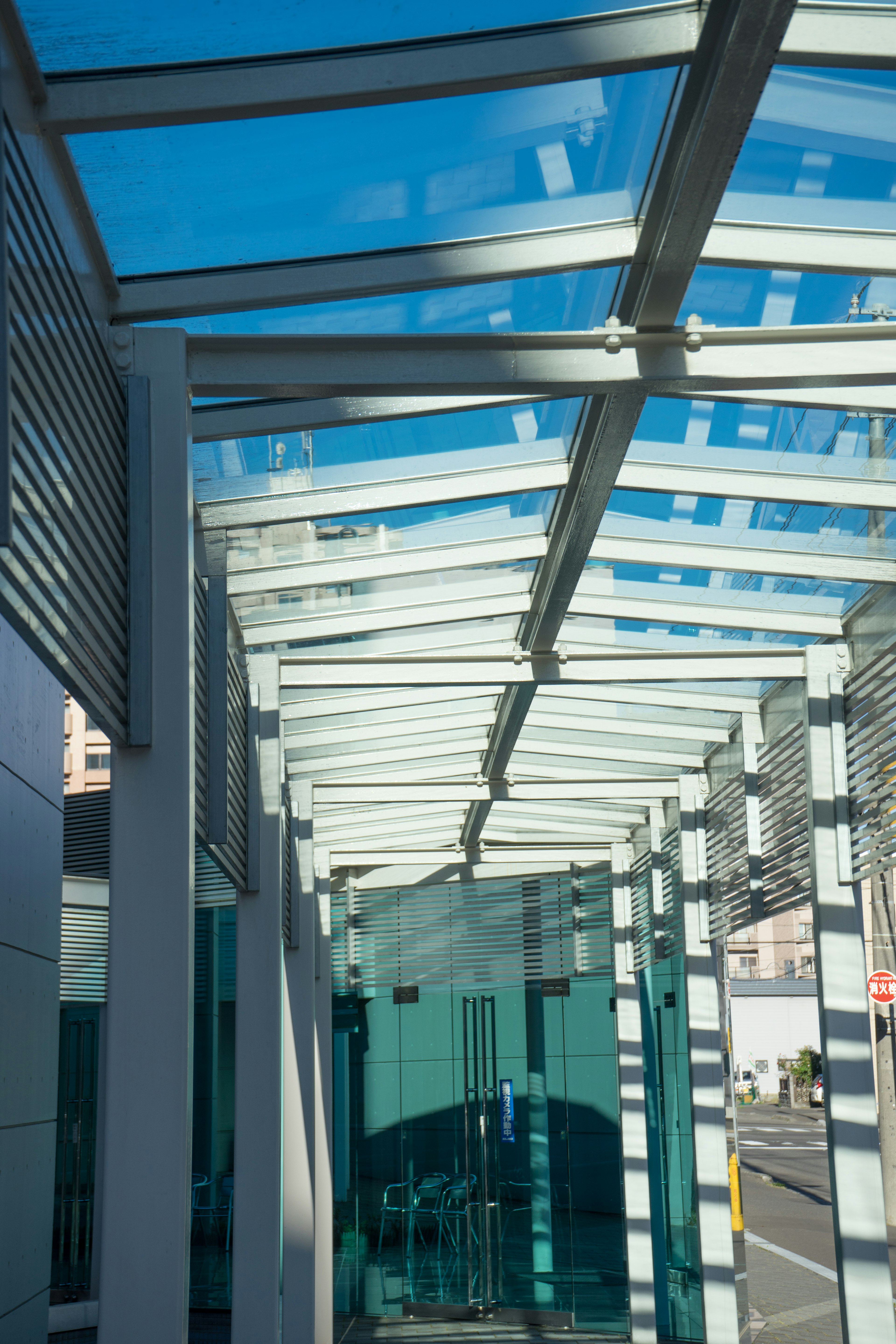 Pintu masuk gedung modern dengan pintu kaca dan atap di bawah langit biru