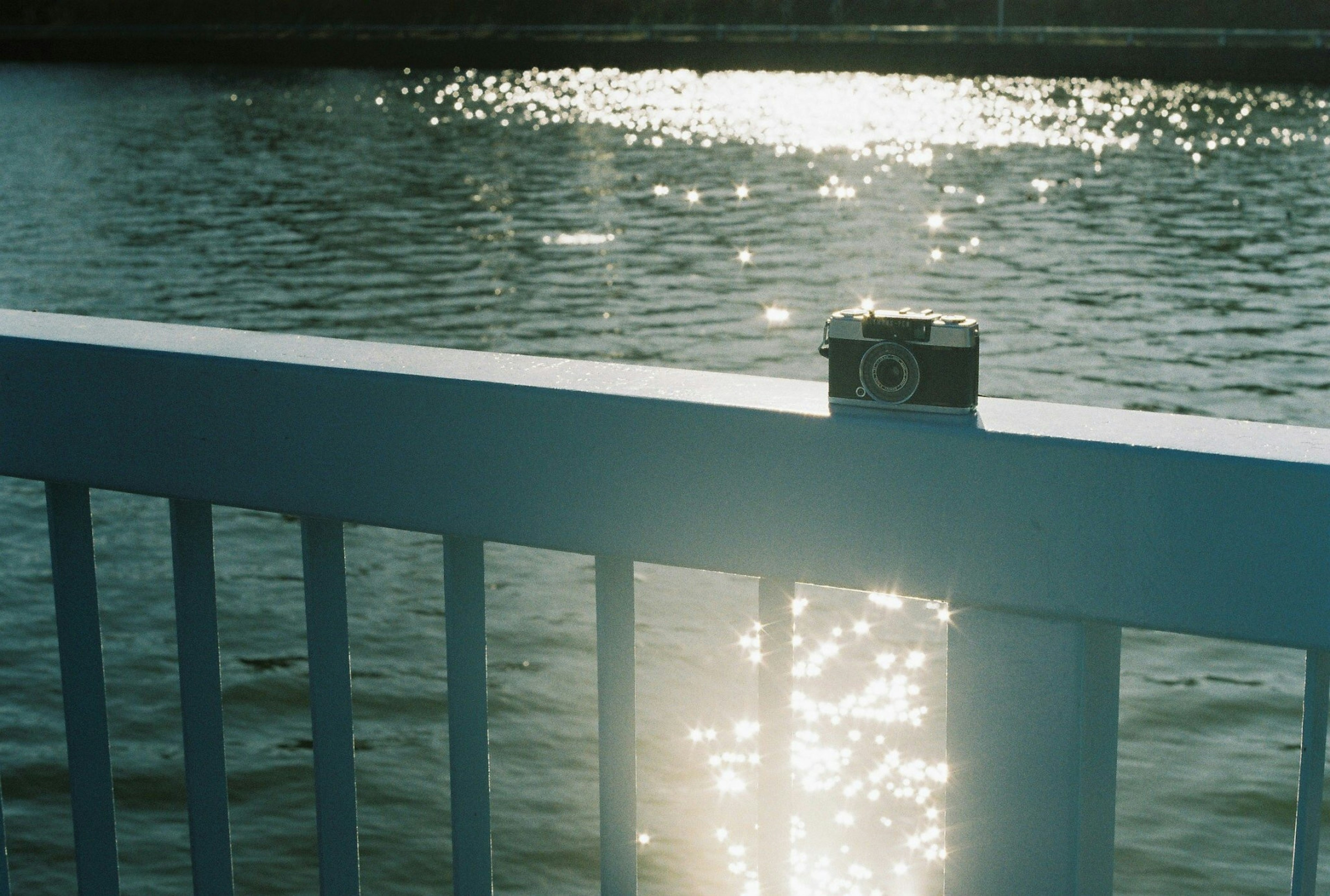 Camera on a white railing with sparkling water in the background