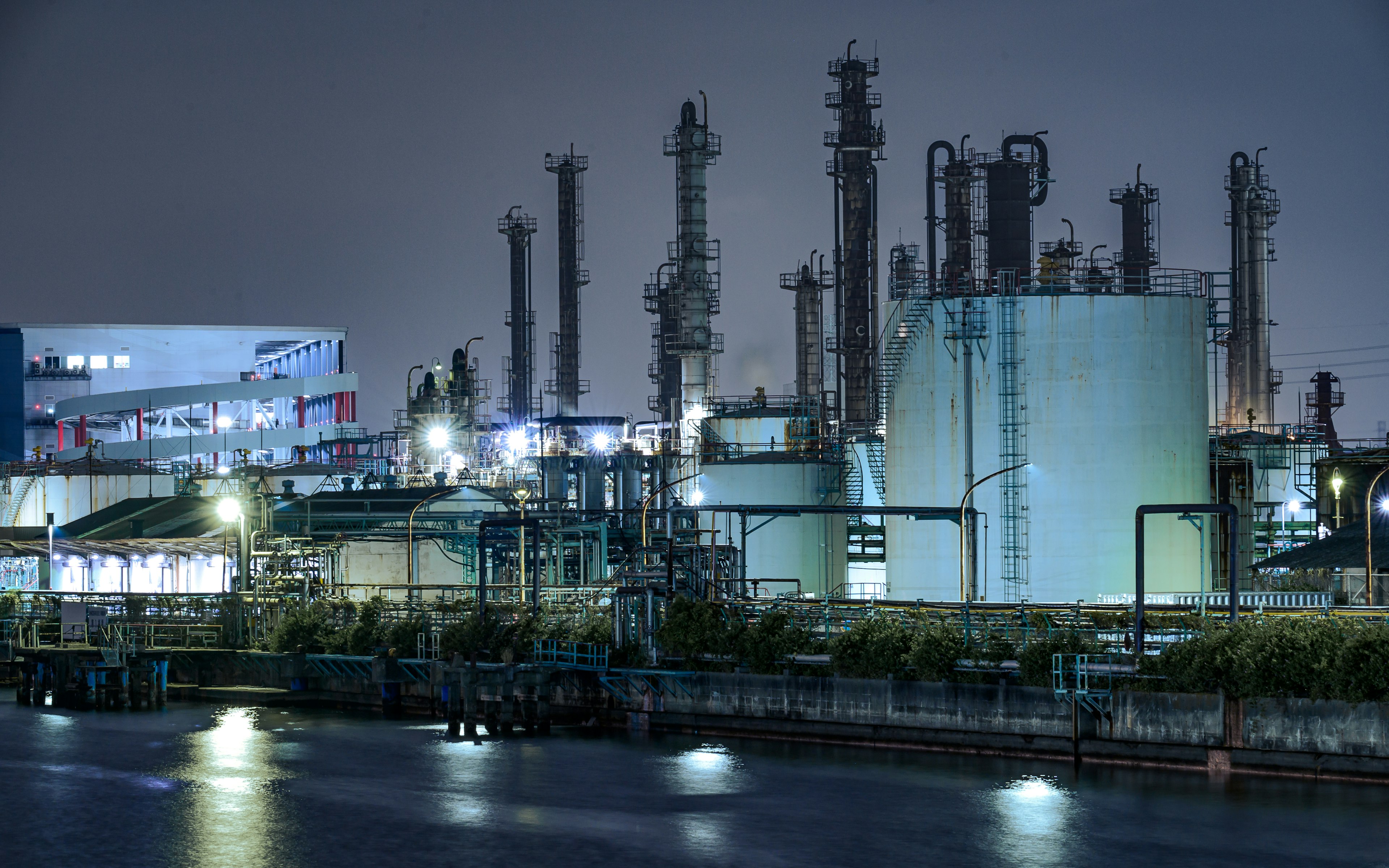 Industrial landscape at night featuring illuminated tanks and smokestacks