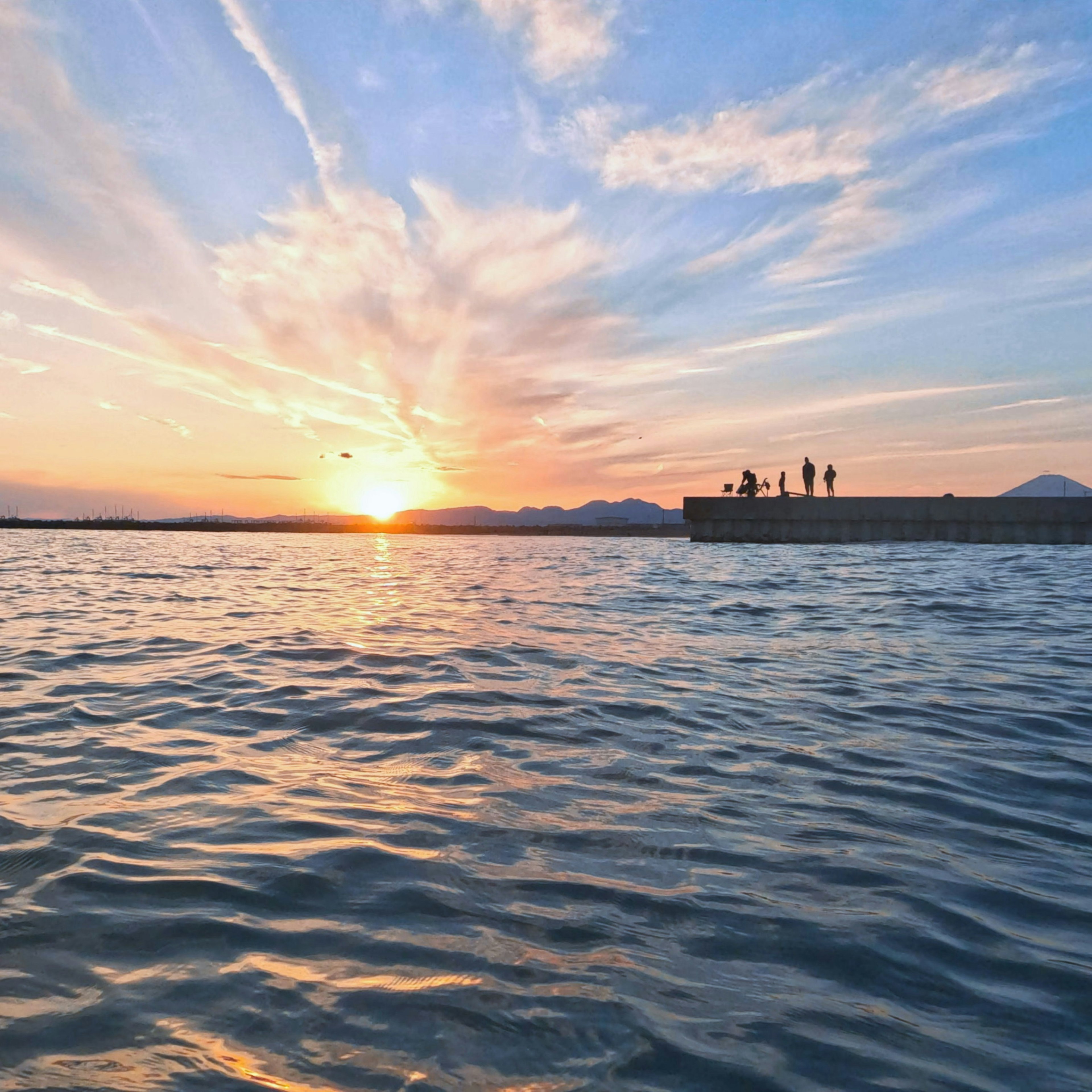 夕日が海に沈む様子と人々がいる岸