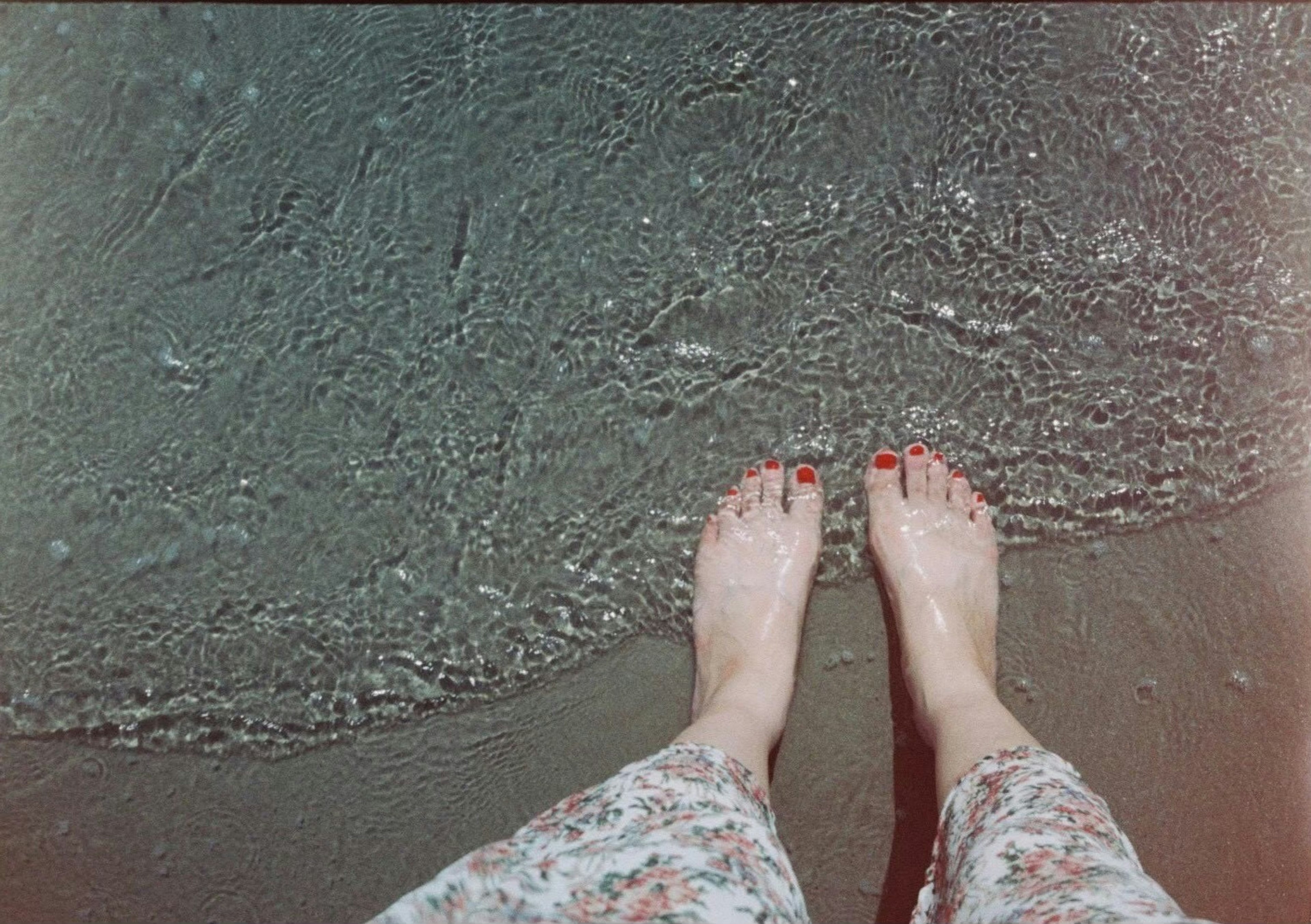 Bare feet touching ocean waves with floral skirt