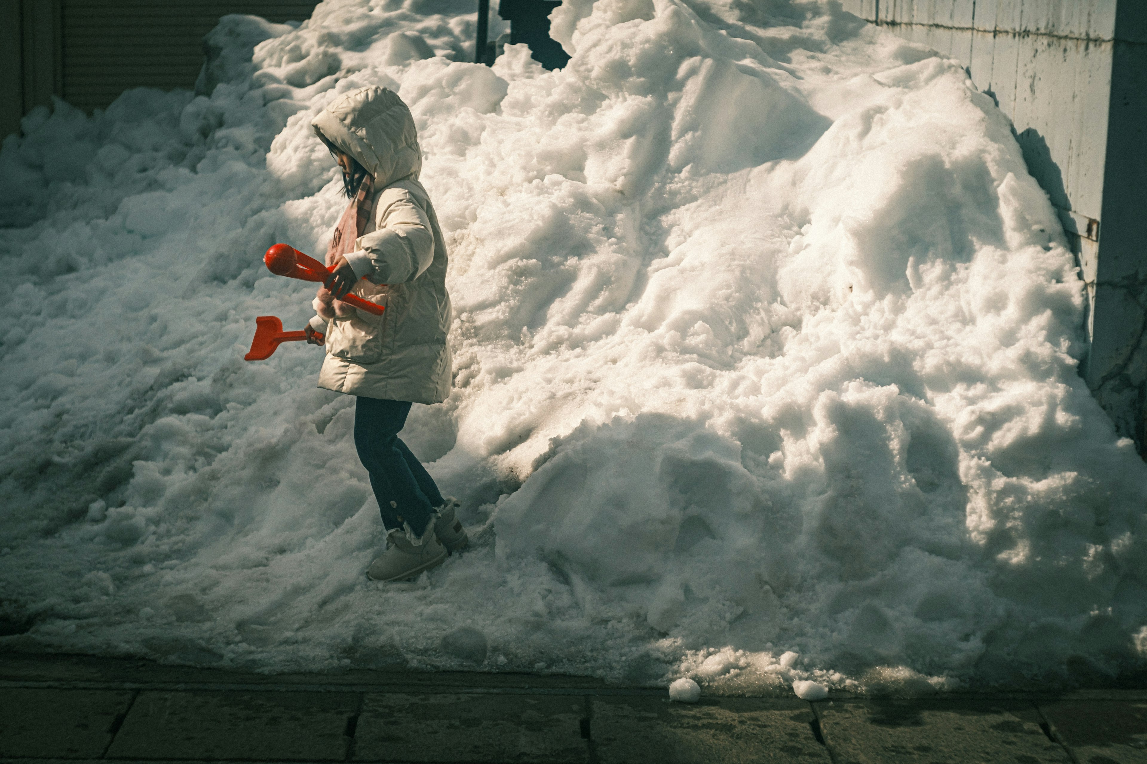 Enfant jouant près d'un tas de neige tenant des pelles rouges portant un manteau blanc