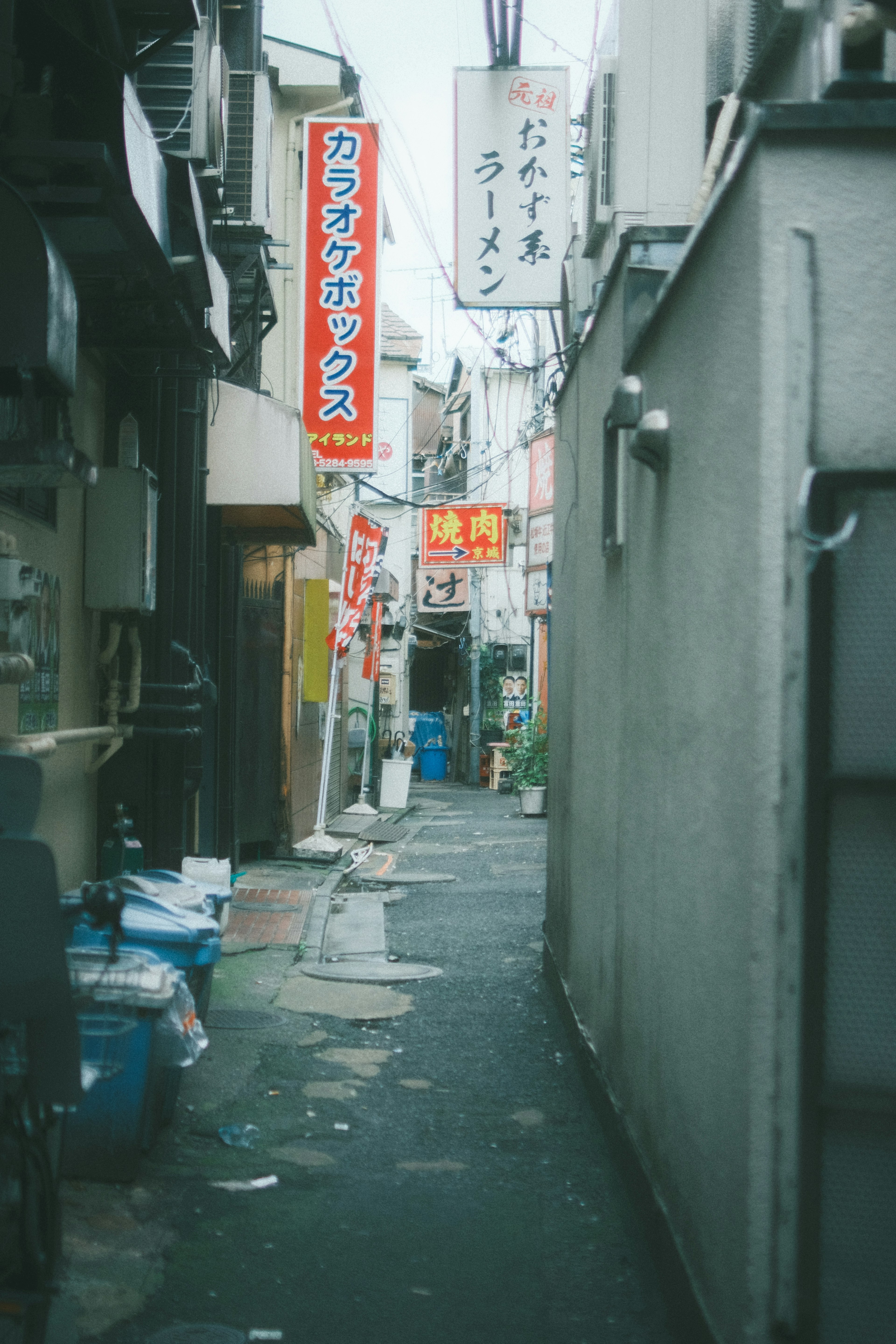 狭い路地に並ぶ飲食店の看板とゴミ箱