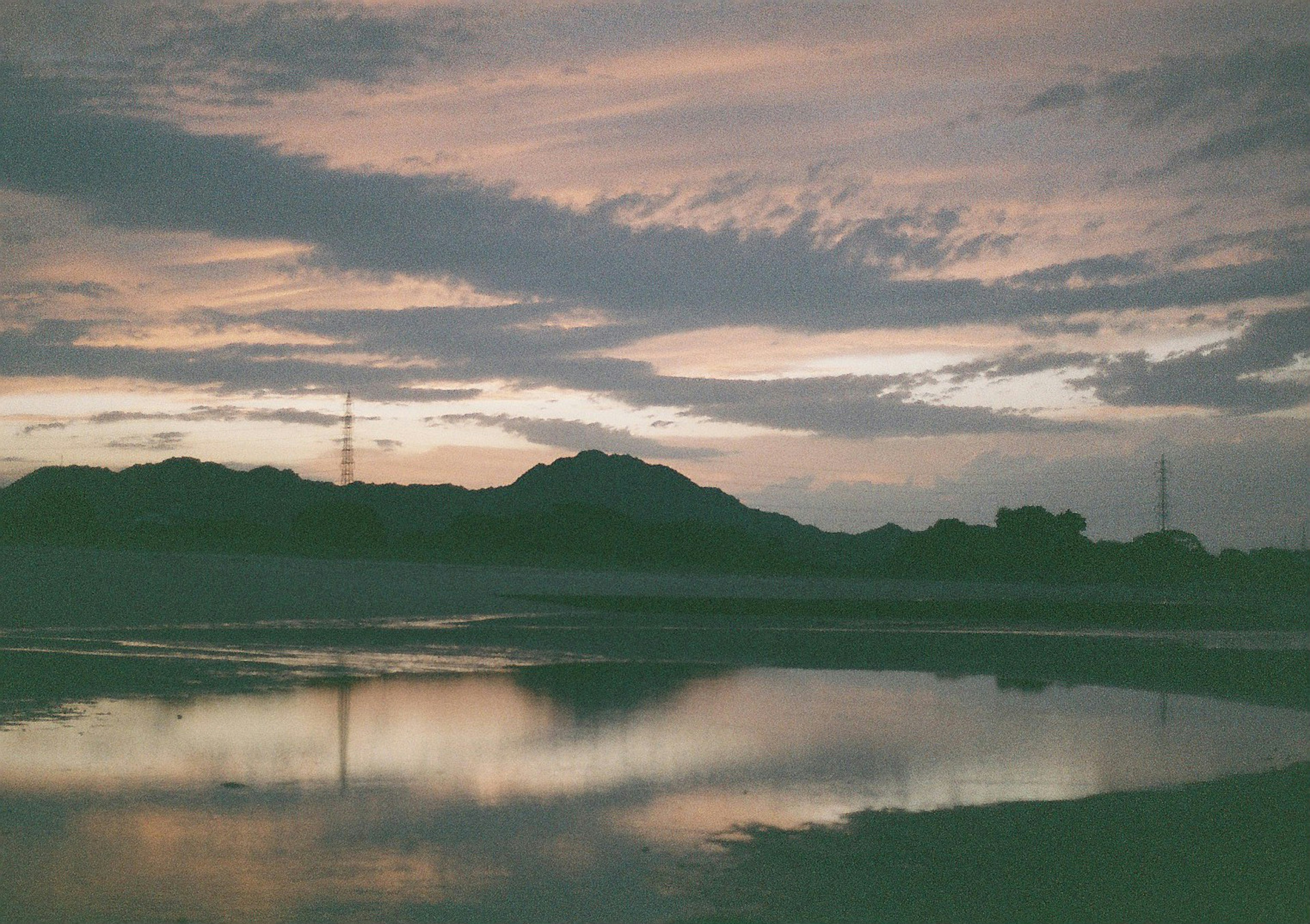 Sunset sky reflecting on water surface with low hills and power poles