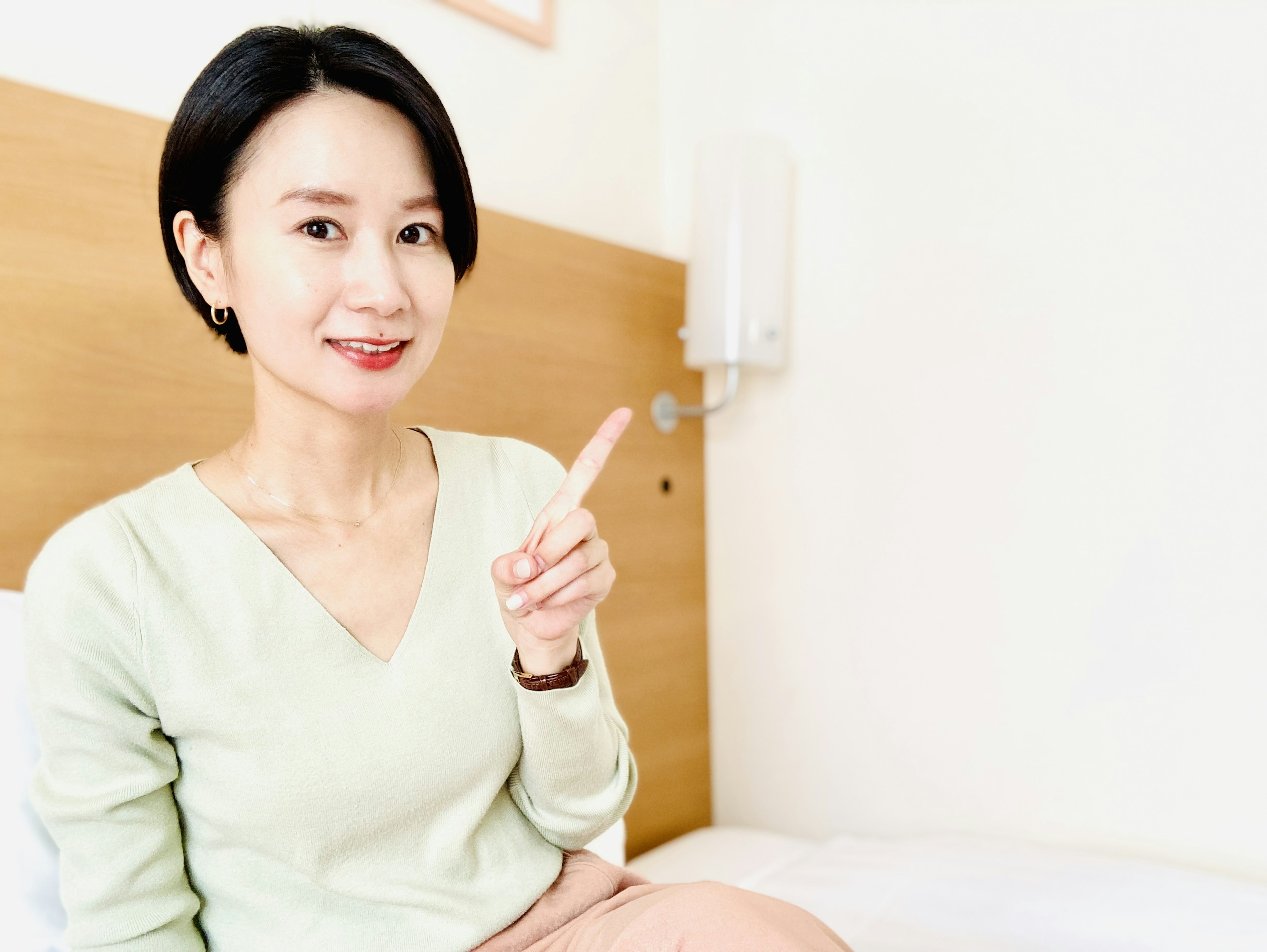 A woman smiling and pointing next to a bed