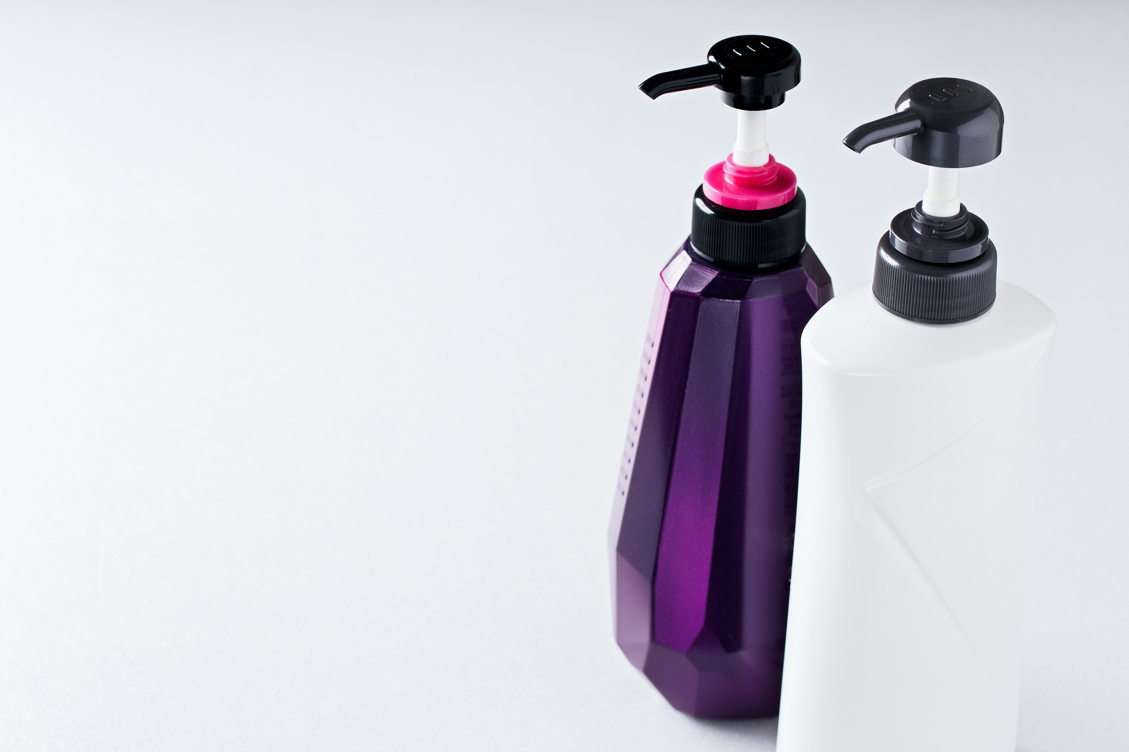 Two pump bottles in purple and white on a minimalist background