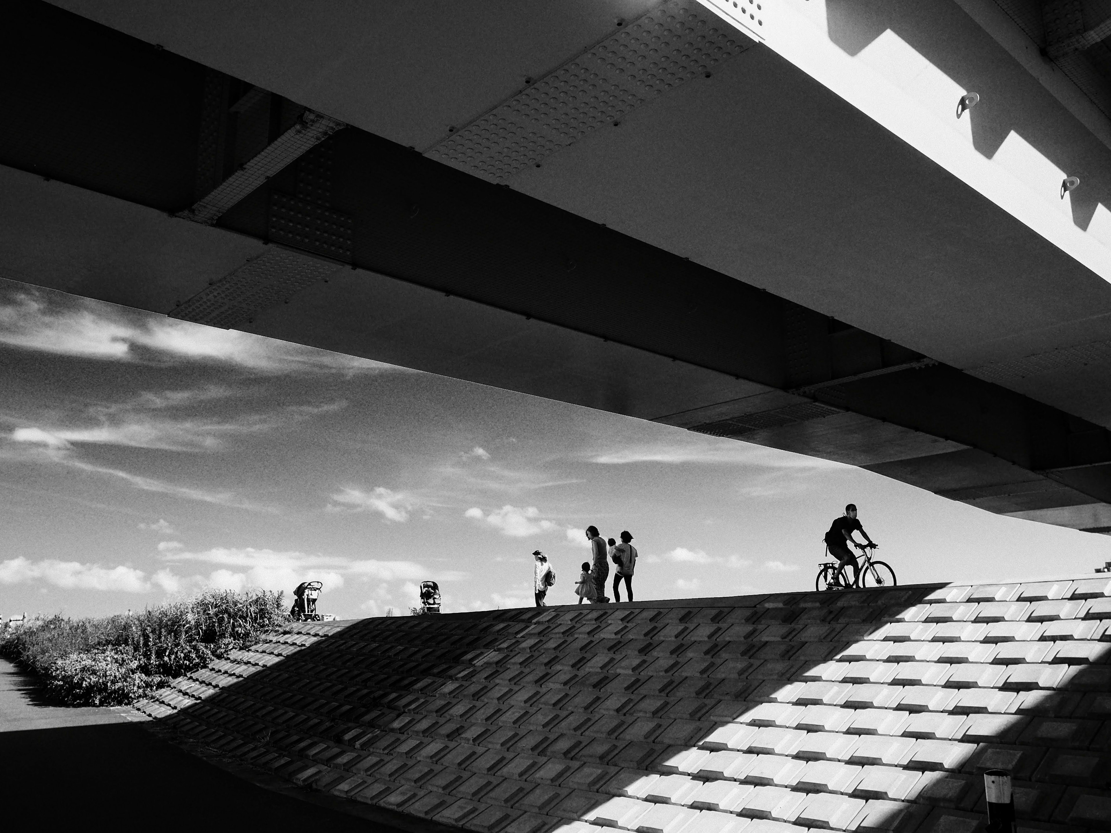 白黒の風景で自転車に乗る人と歩く人々が橋の下にいる