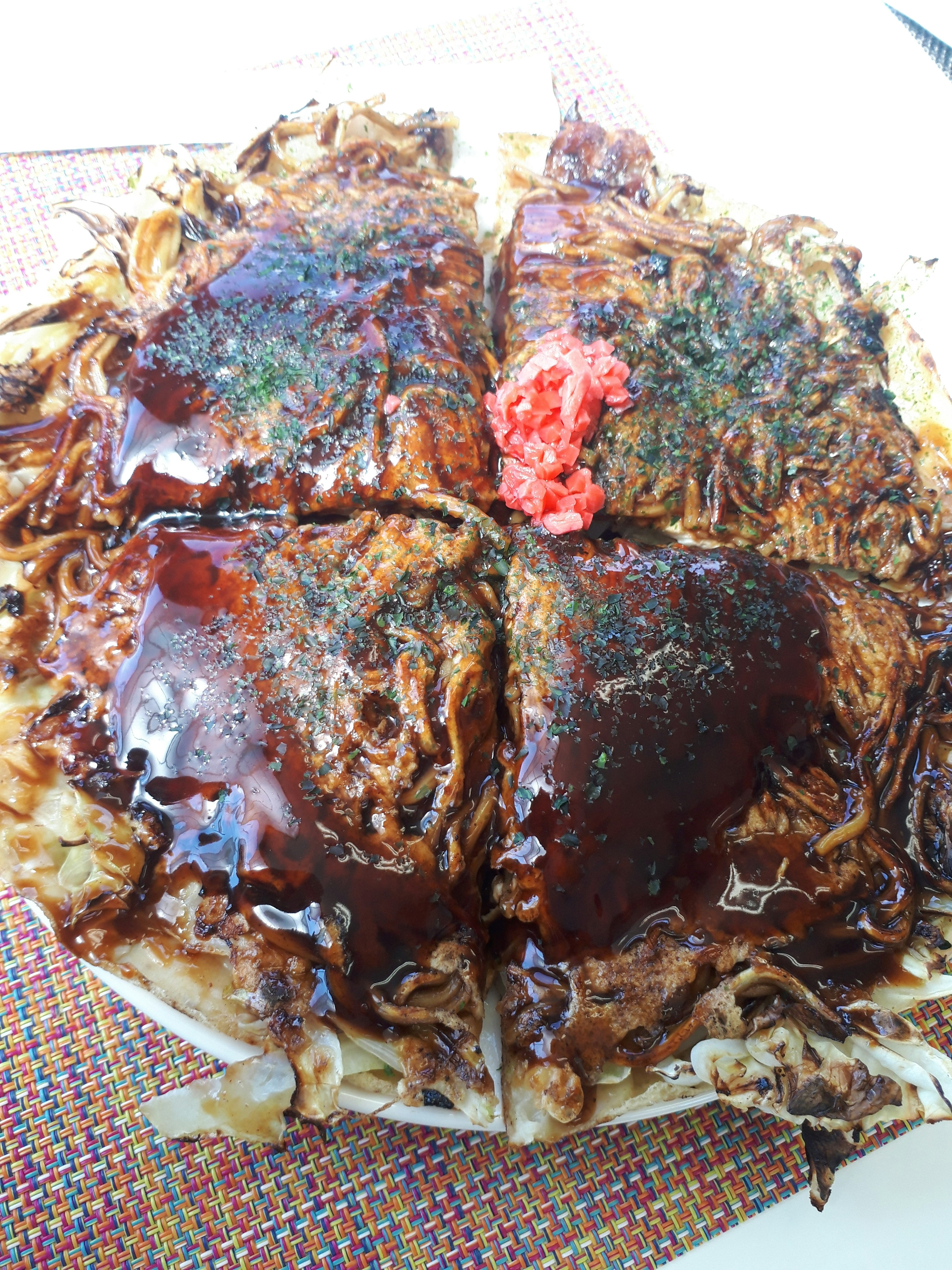 Okonomiyaki disajikan dengan saus, rumput laut, dan jahe acar di atas piring