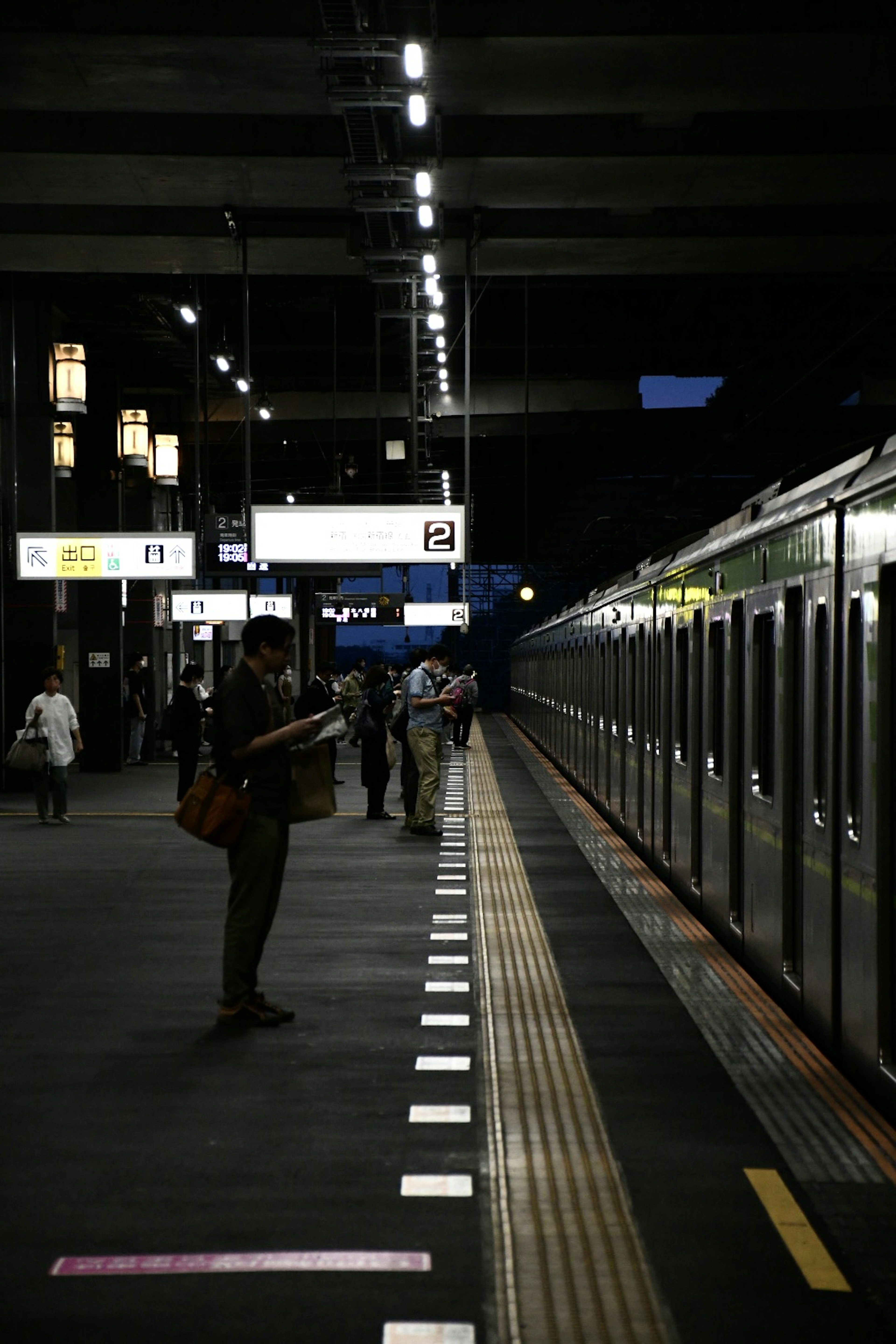 暗い駅のプラットフォームで電車を待つ人々と照明