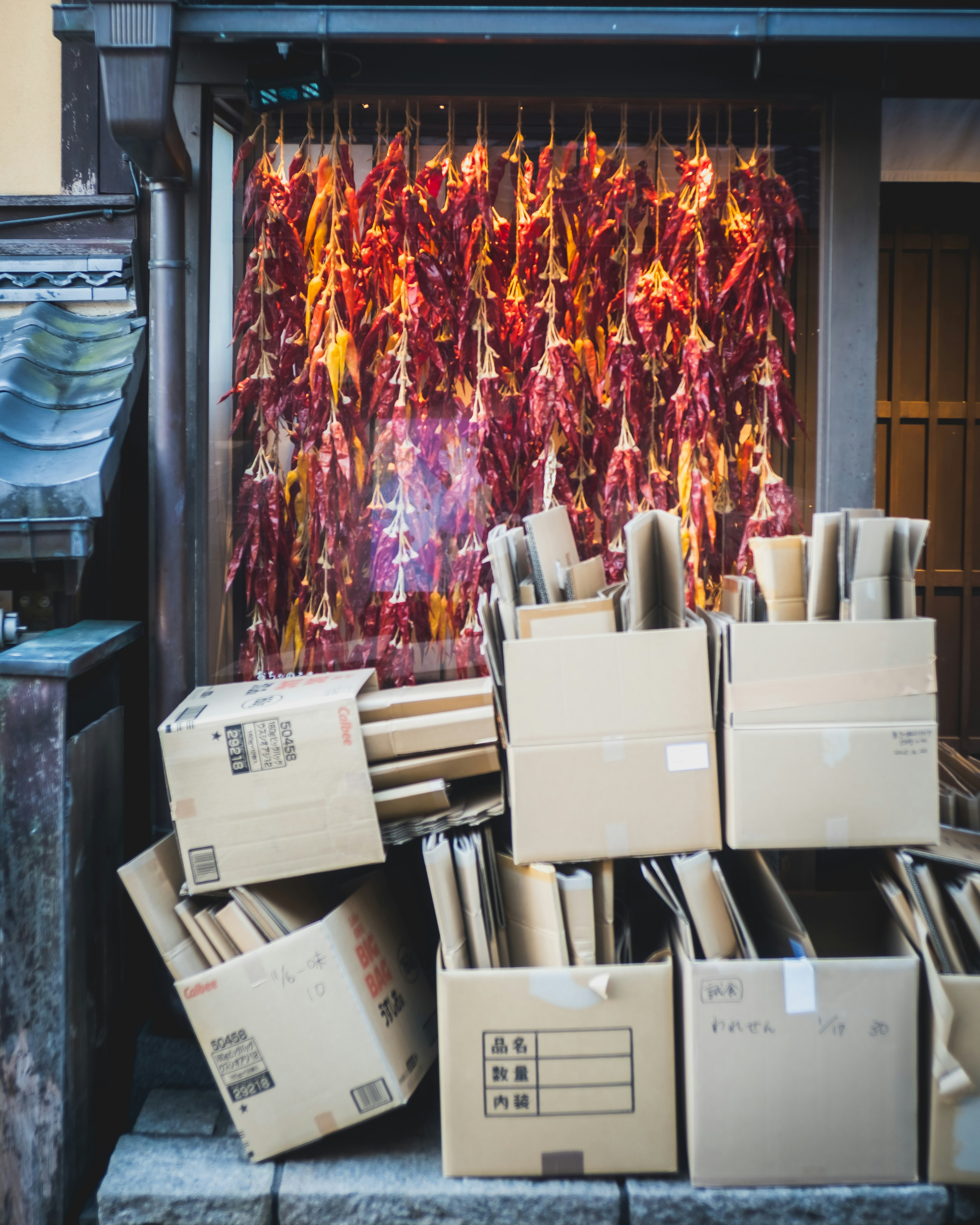 Stack of cardboard boxes in front of an old Japanese shop with dried red chili peppers