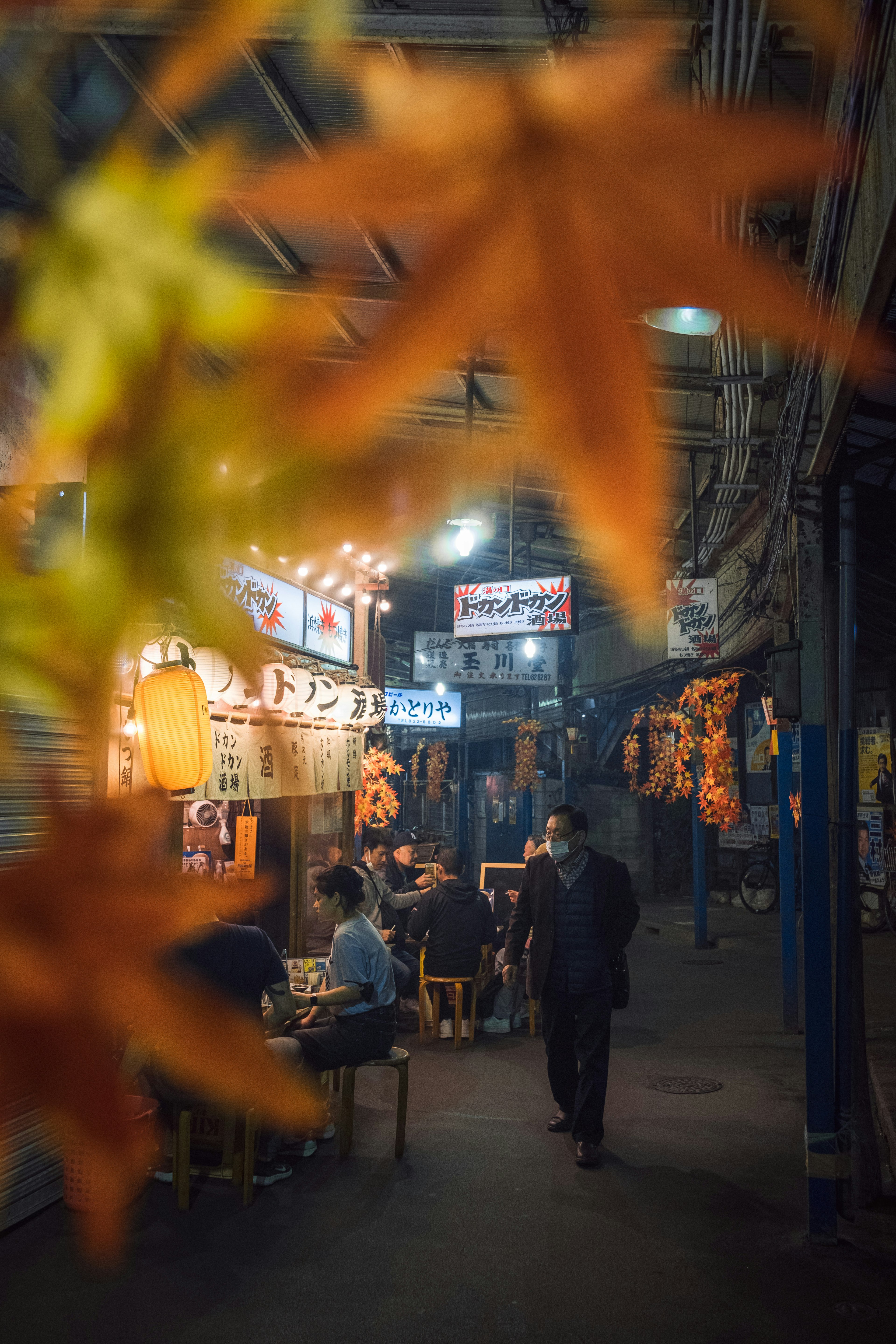 秋の葉が前景にあり、賑やかな屋台が並ぶ夜の市場の風景