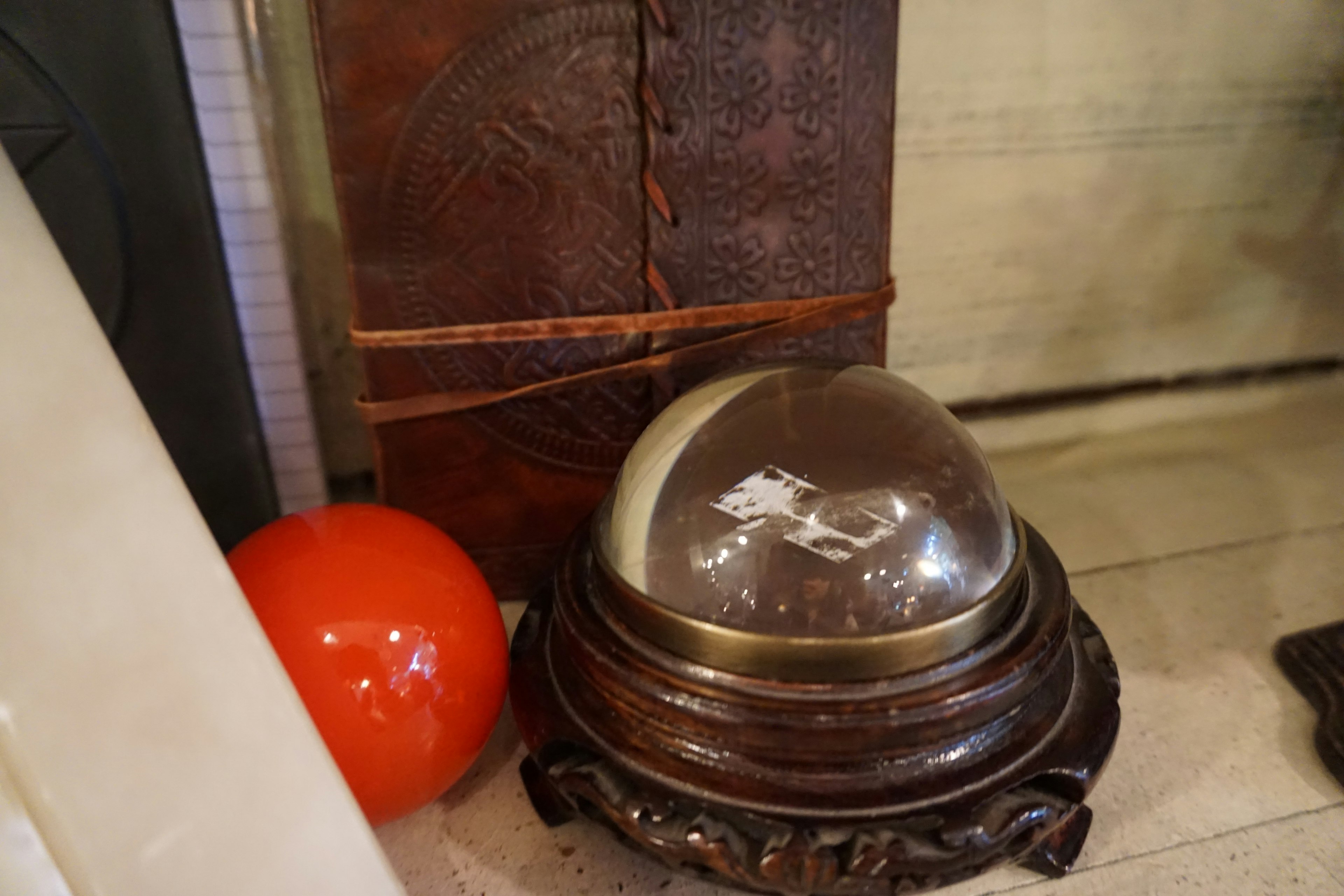 Transparent dome object on decorative wooden base beside a red sphere and a leather-bound book