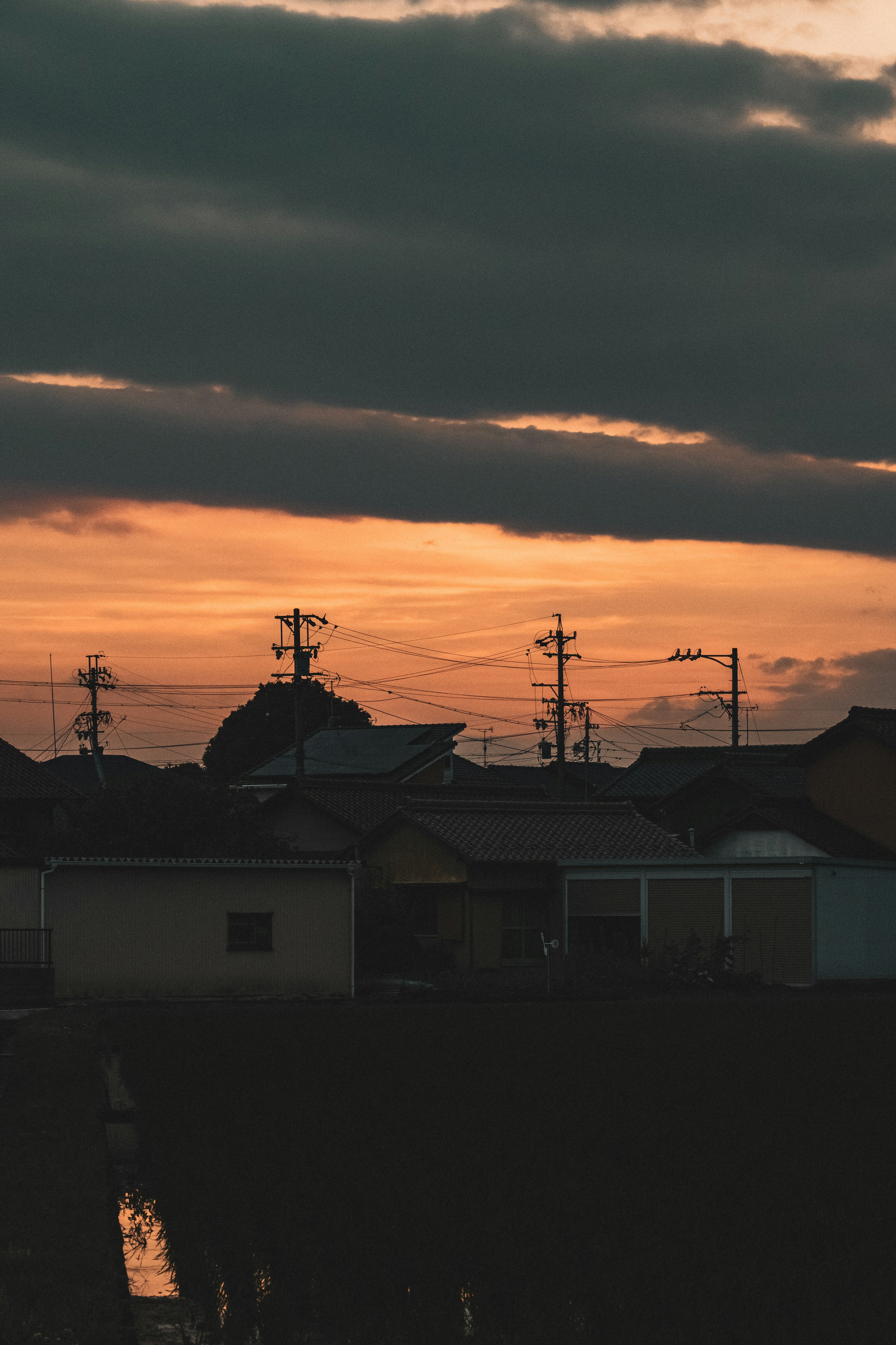 夕焼けの中に silhouetted な家々と電柱が見える風景