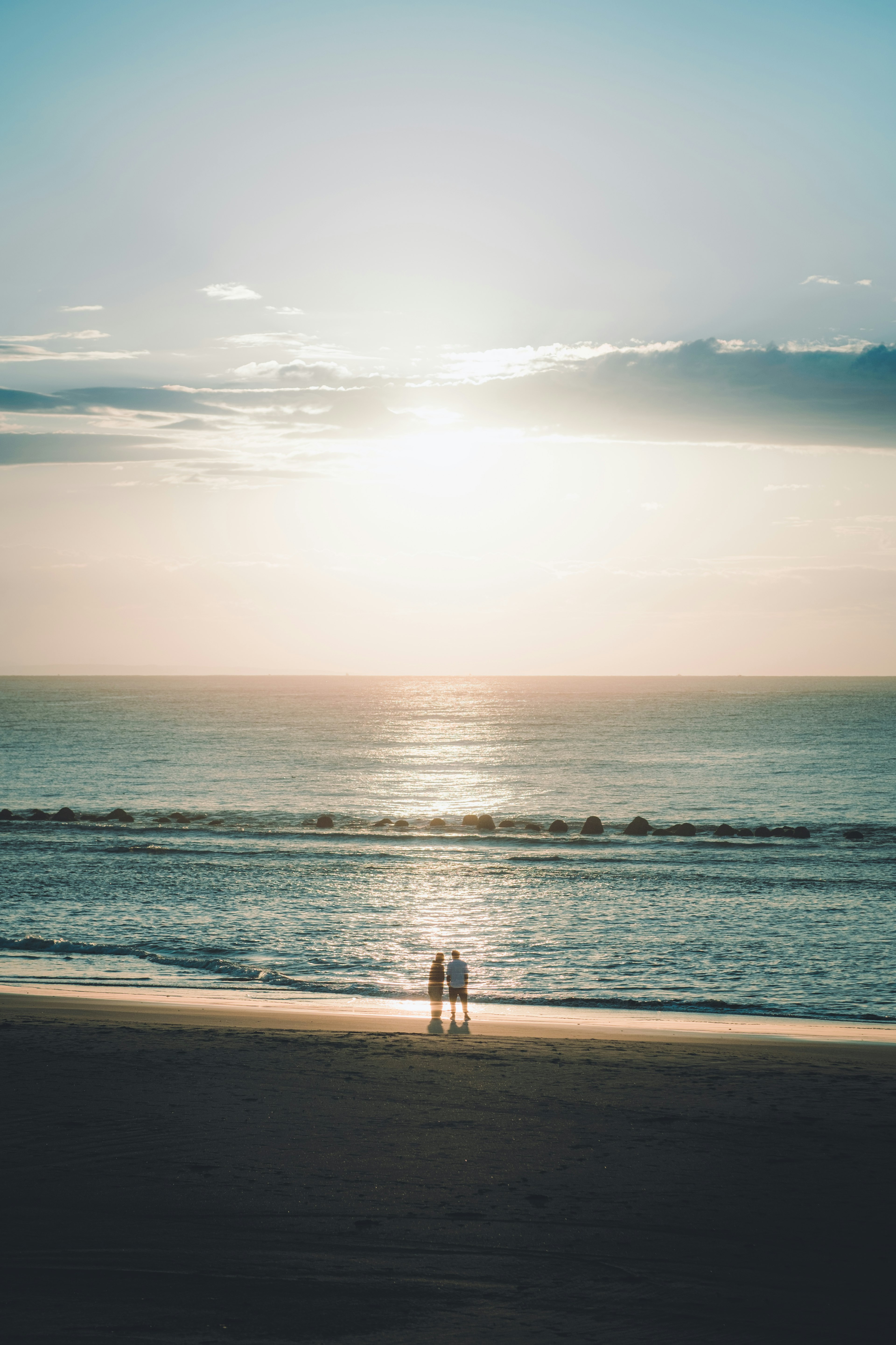 Silueta de dos personas de pie en una playa con un atardecer de fondo