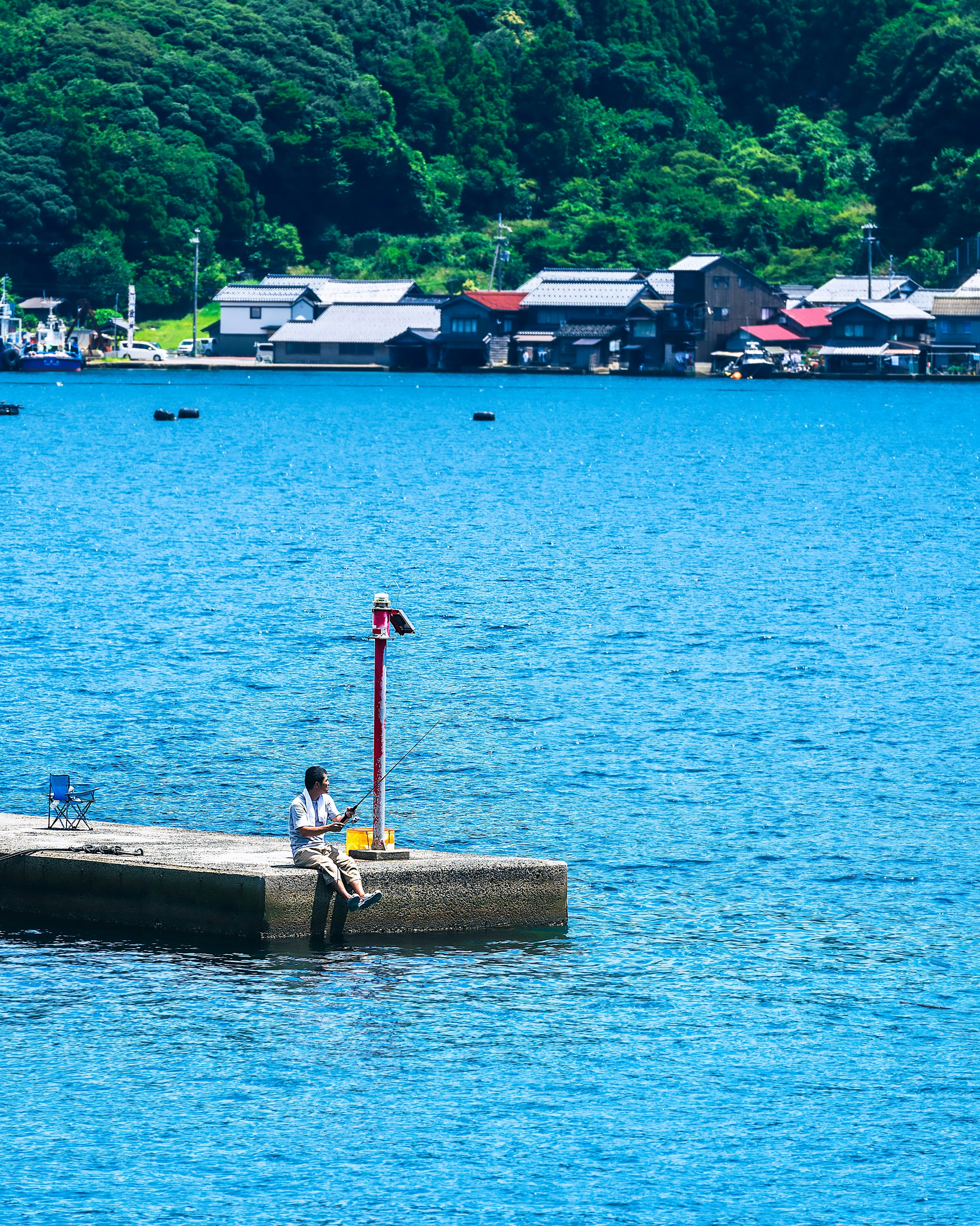 Persona sentada en un muelle con agua azul y casas pequeñas al fondo